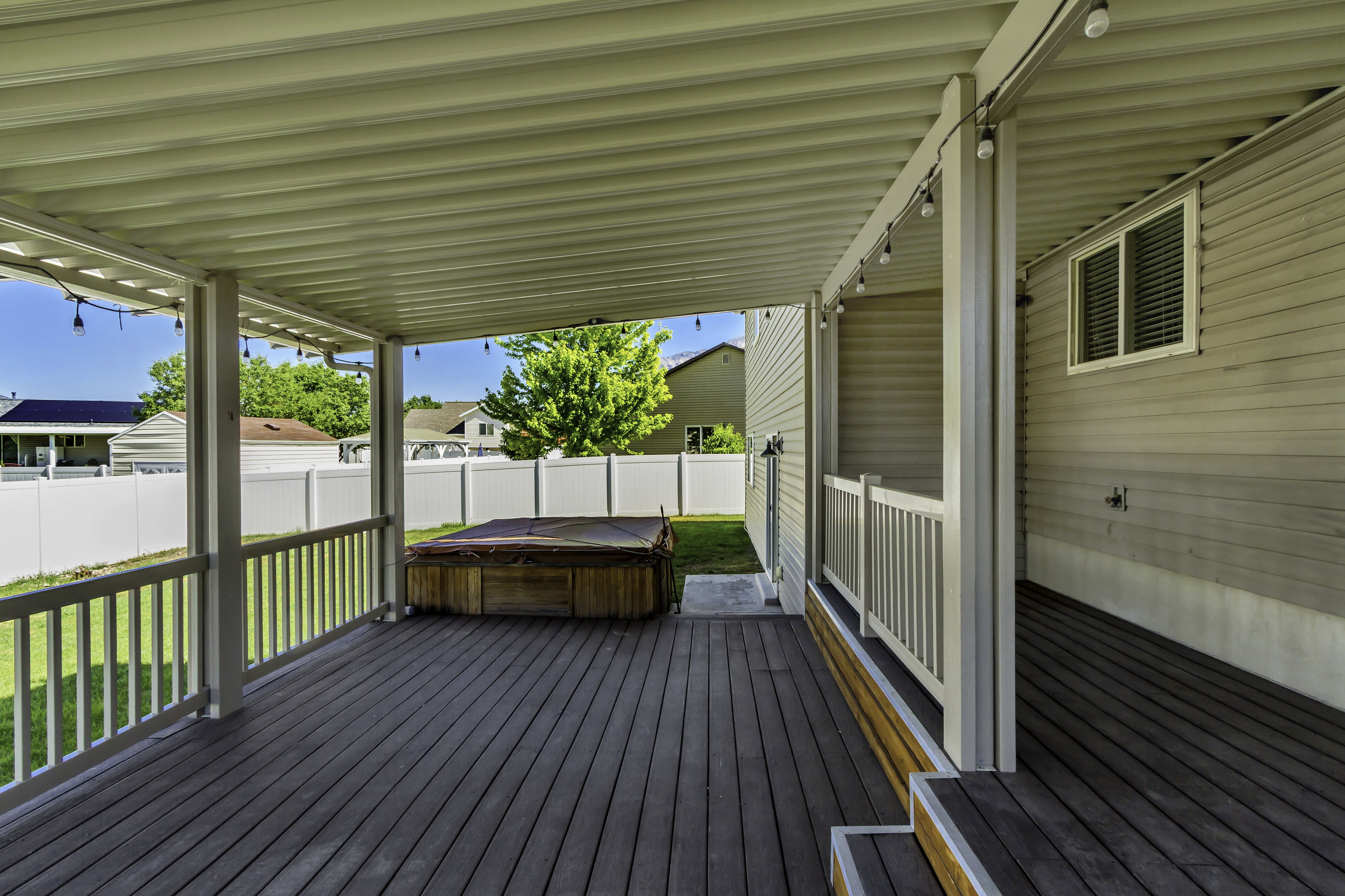 Expansive covered deck featuring composite decking, a built-in spa, white vinyl railing, and exterior lighting
