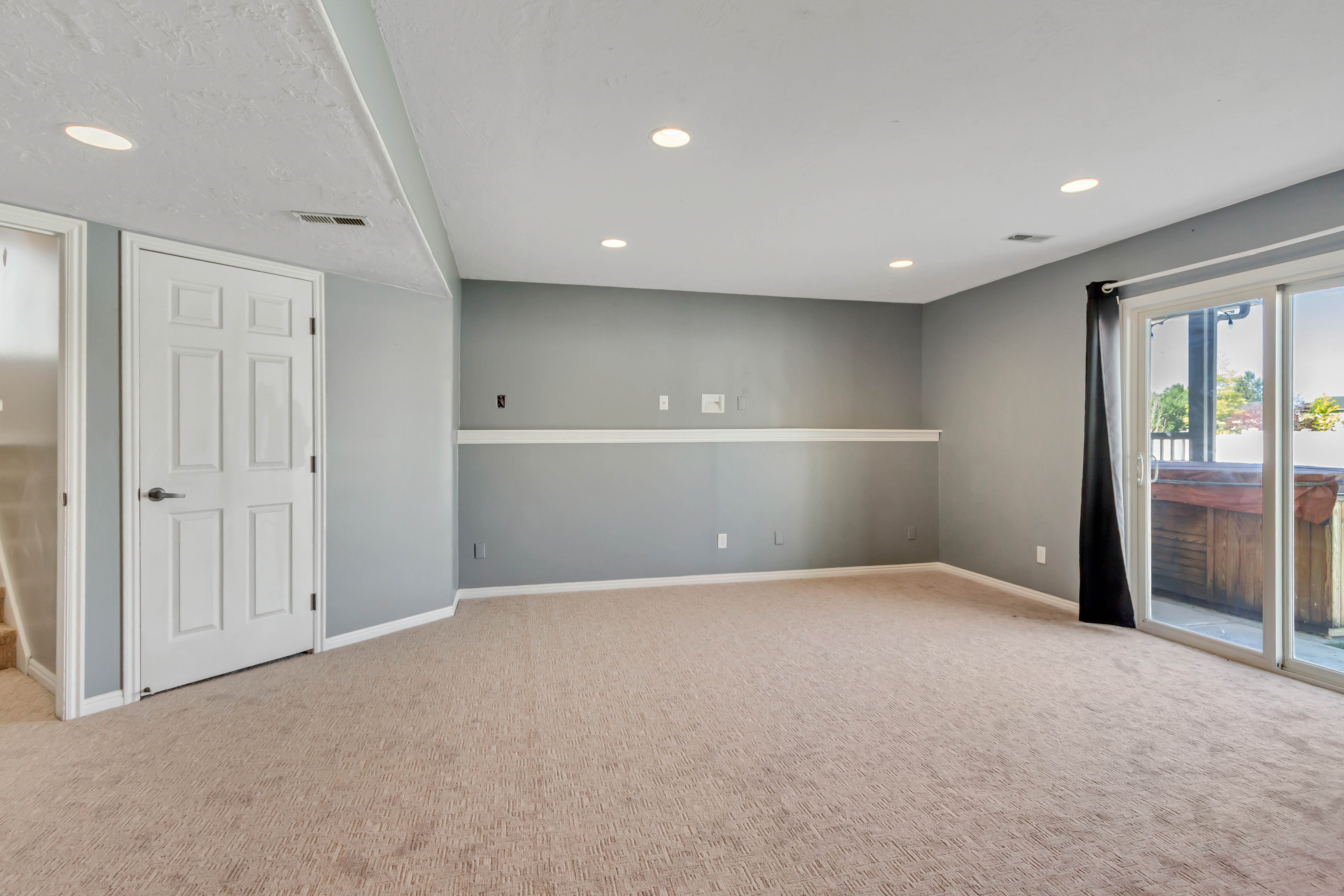 Spacious carpeted room featuring recessed lighting, a sliding glass door providing exterior access, a visible hot tub on the patio, and a paneled interior door