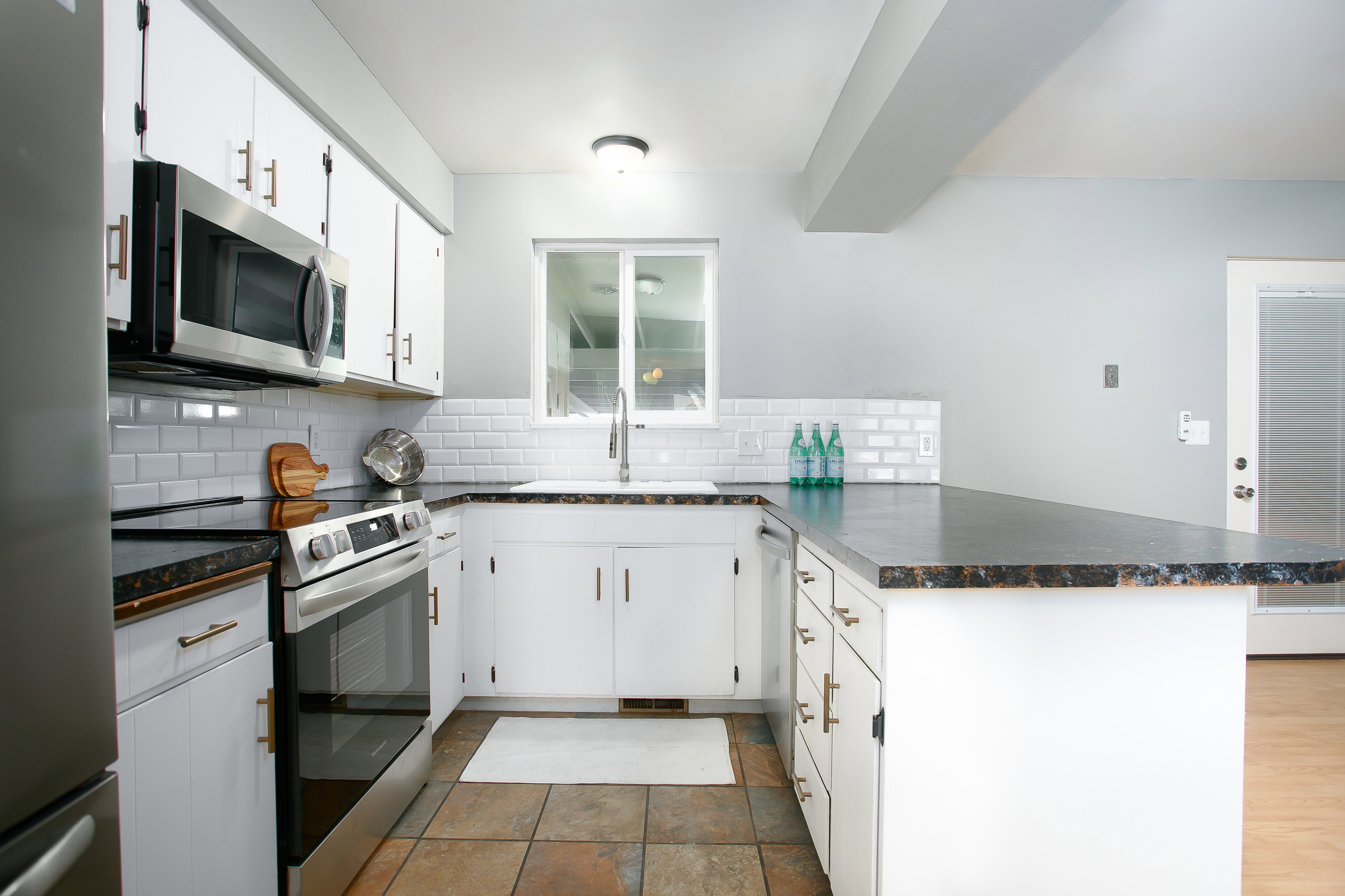 Kitchen featuring white cabinetry, stainless steel appliances, dark stone-finish countertops, white subway tile backsplash, and tile flooring