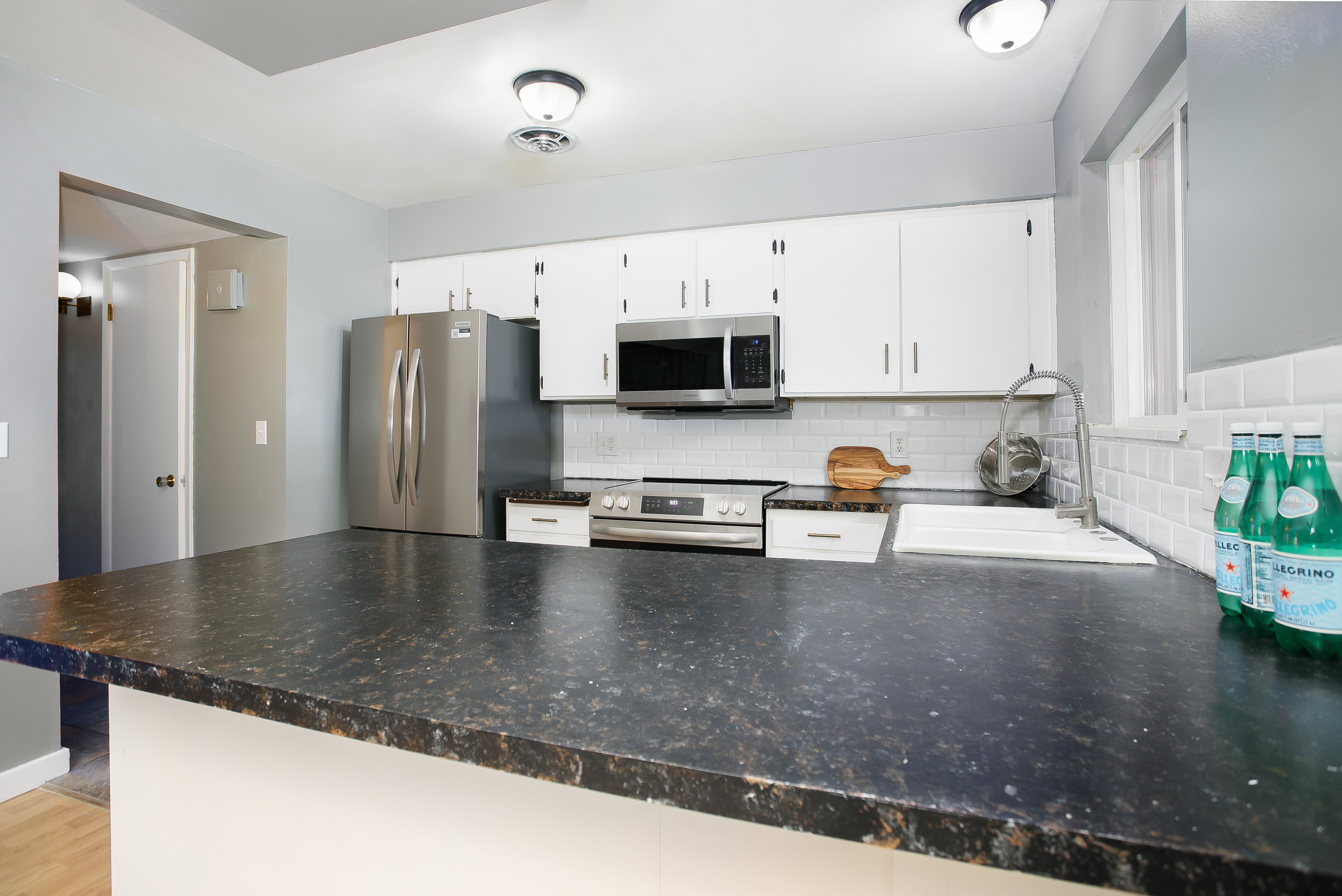 Expansive dark stone-finish countertop with white cabinetry, stainless steel appliances, white subway tile backsplash, and an undermount sink