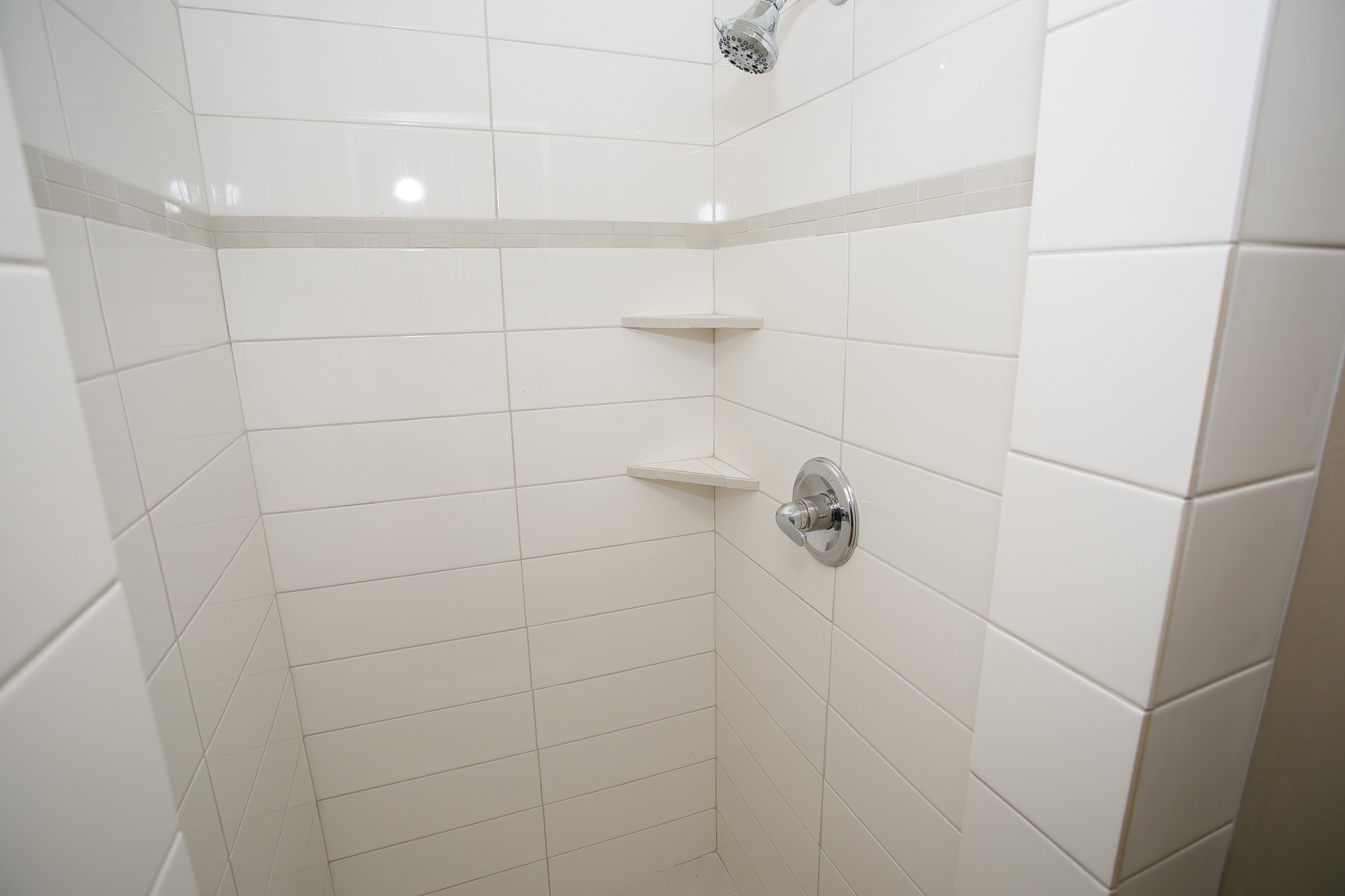 Tiled shower enclosure featuring white subway tile, a chrome showerhead, and integrated corner shelving