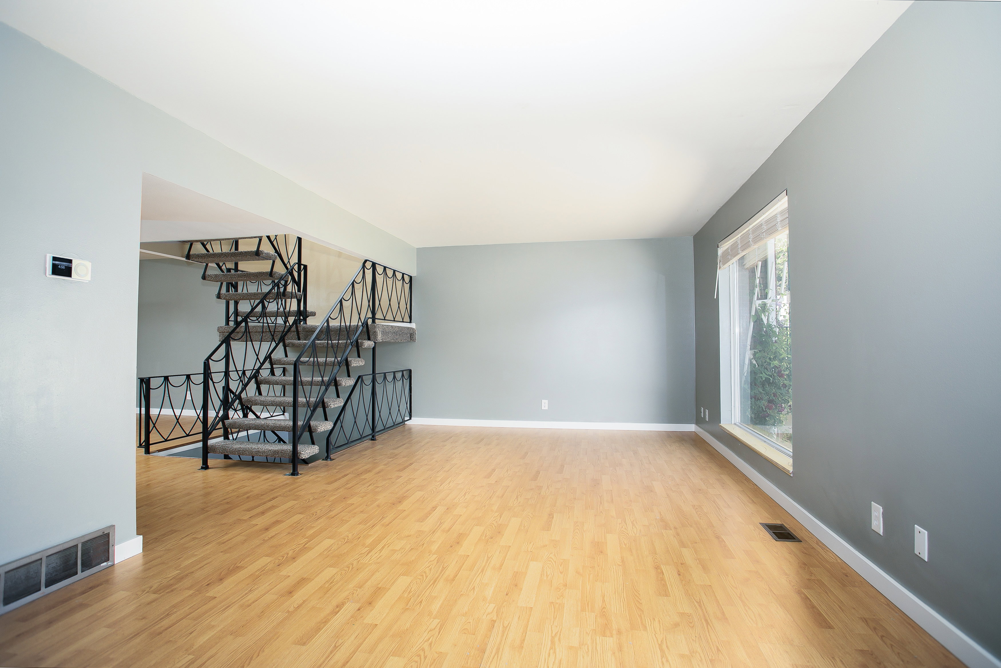 Spacious interior featuring a multi-level staircase with decorative metal railings, light wood-finish flooring, a large picture window, and neutral wall tones