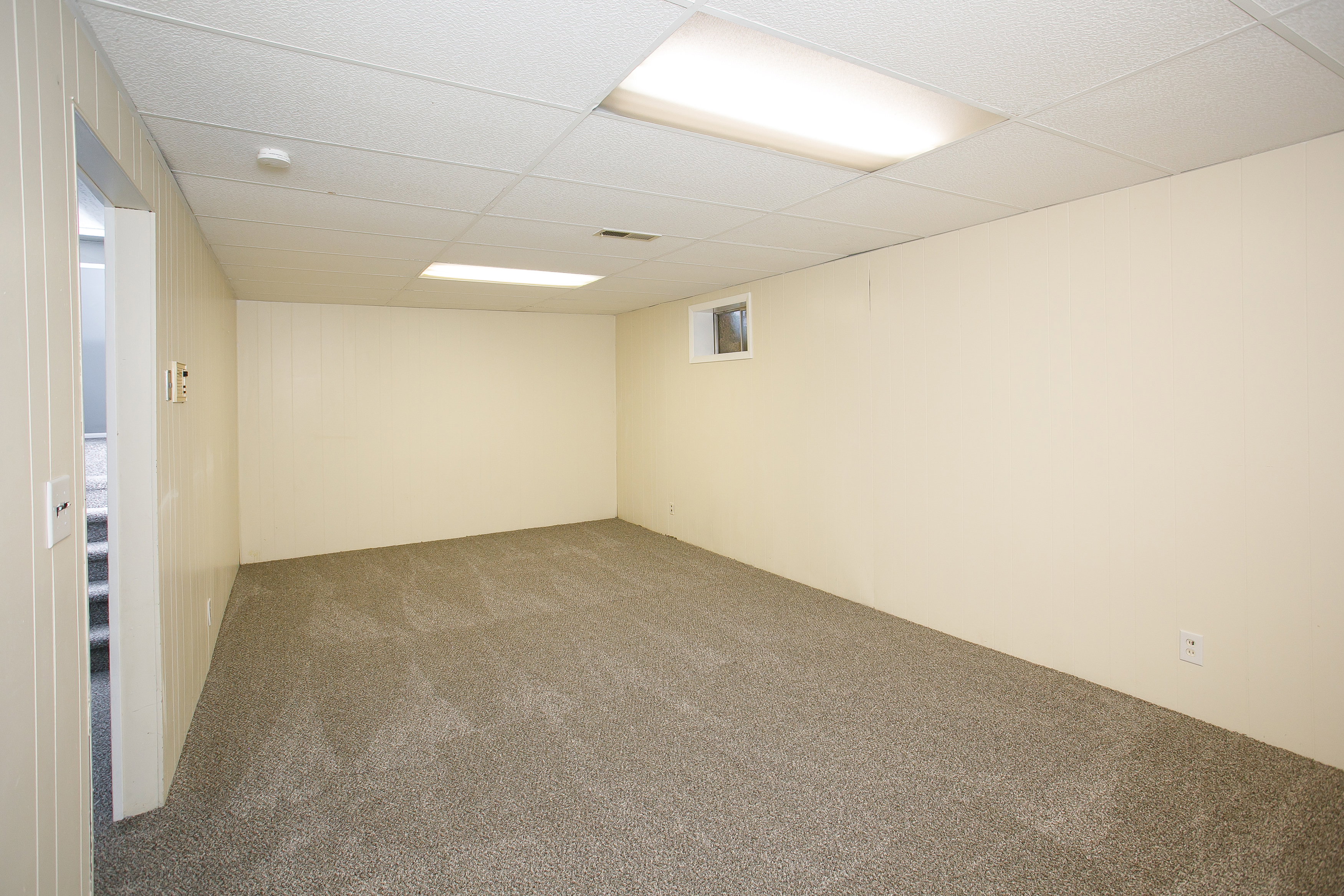 Spacious room featuring neutral carpeting, light-toned walls, and a drop ceiling with integrated lighting