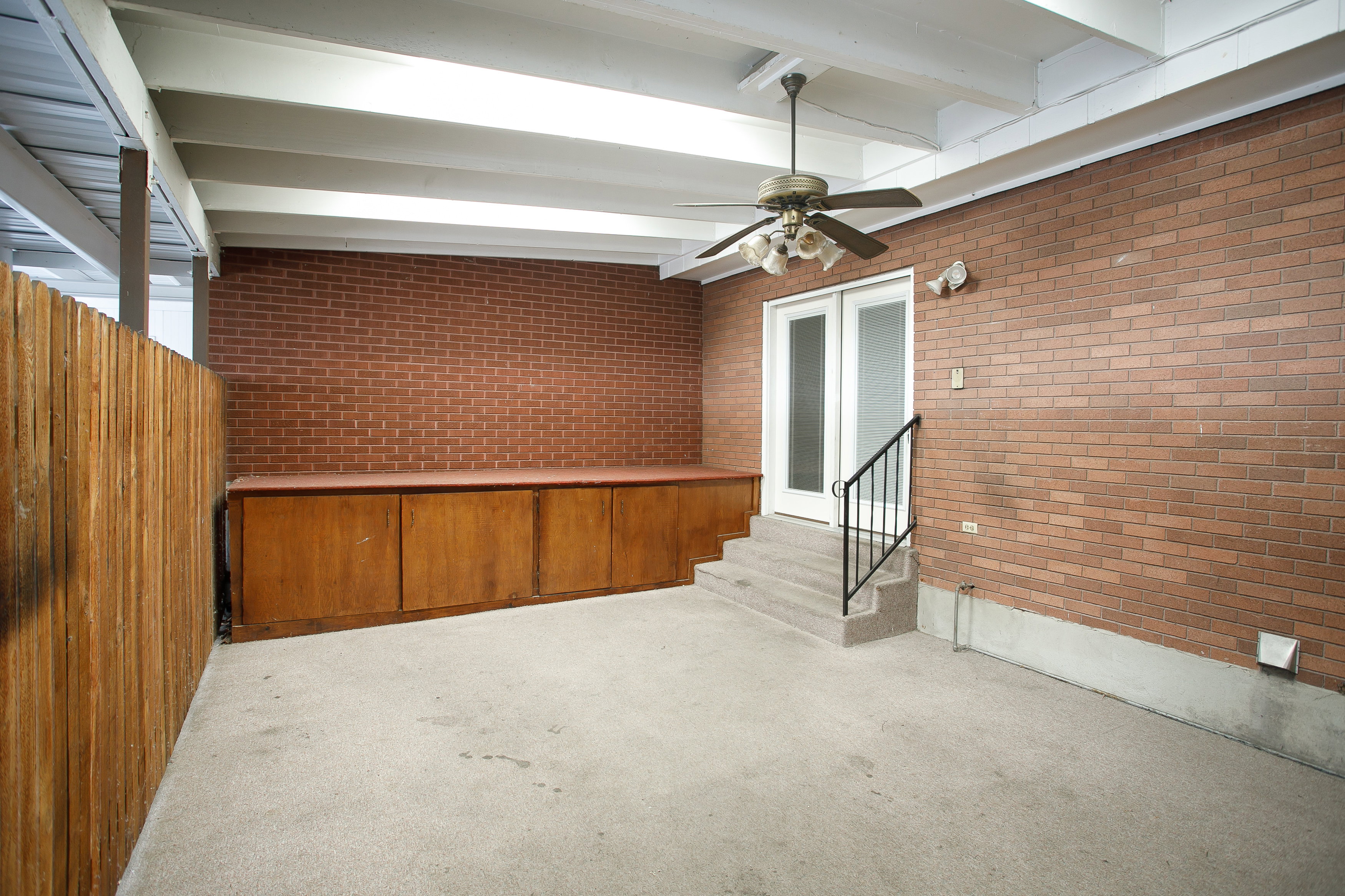 Covered patio featuring a brick wall, wood paneling, and a ceiling fan with integrated lighting