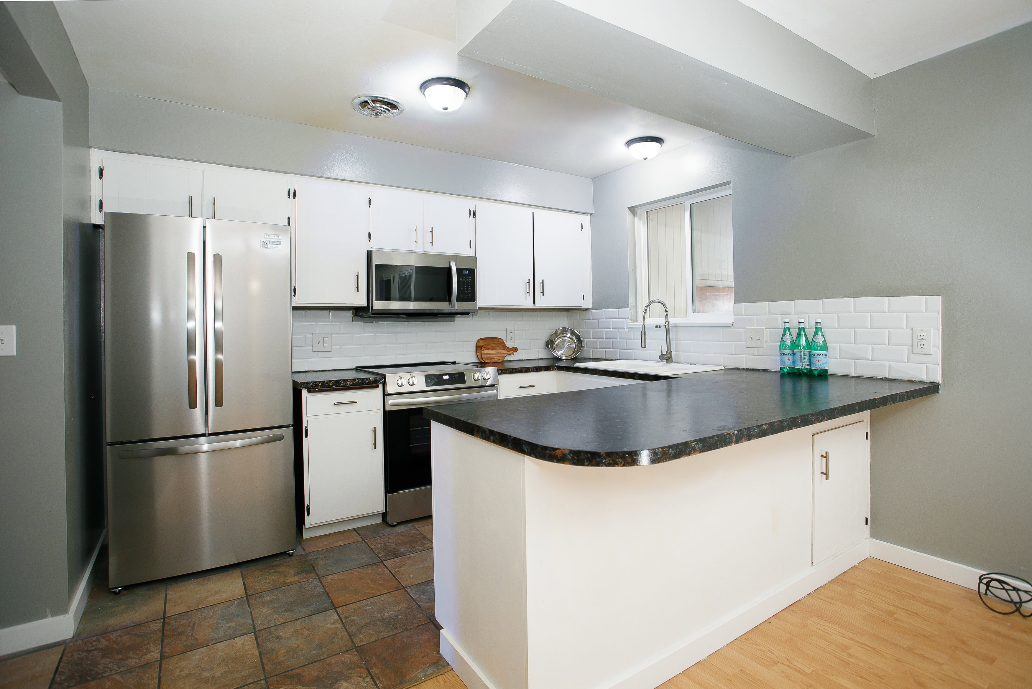 Kitchen featuring a stainless steel French door refrigerator, white cabinetry, dark countertops, a white subway tile backsplash, and multi-toned tile flooring