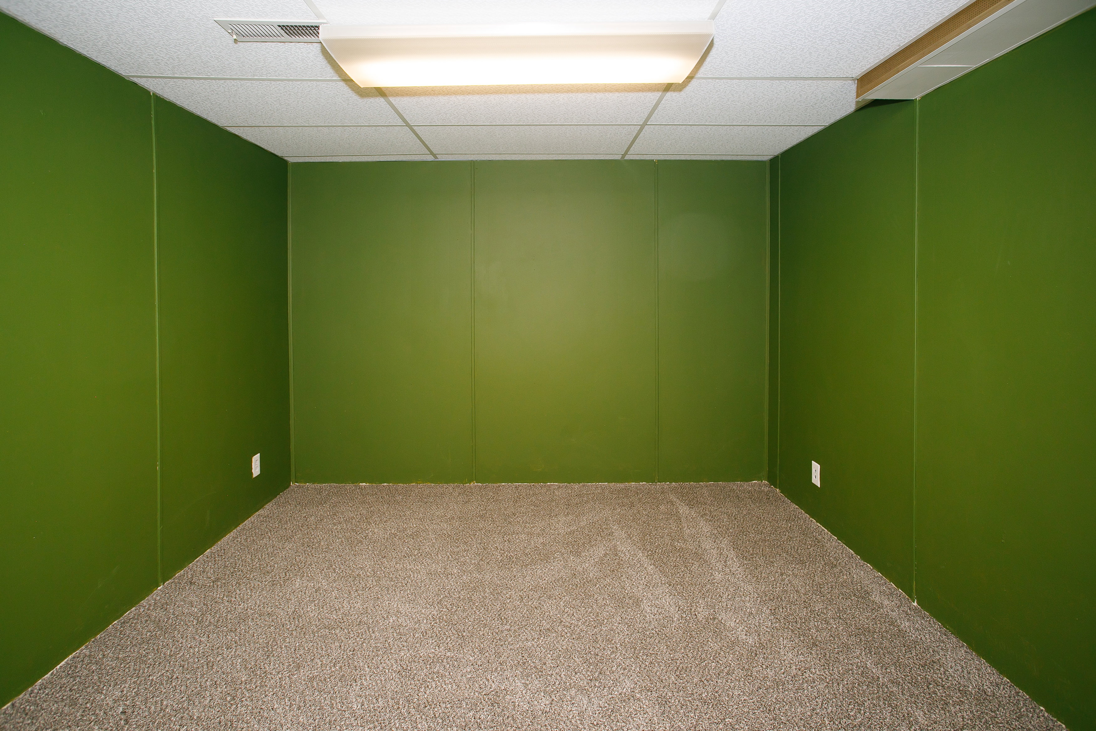 Carpeted room with green panel walls and a drop ceiling featuring recessed lighting
