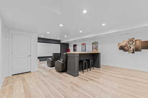 Spacious entertainment area featuring wood-finish flooring, recessed lighting, and a built-in bar with a wooden countertop