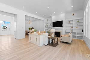 Spacious living area featuring light wood-finish flooring, a fireplace with a white mantel, and built-in shelving
