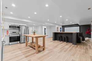 Open-concept entertainment space featuring light wood-finish flooring, recessed lighting, and a white ceiling