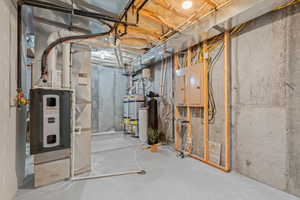 Utility area featuring a furnace system, multiple water heaters, a water filtration system, exposed concrete walls, and electrical panels