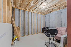 Unfinished basement with concrete walls, exposed wood framing, and ceiling insulation