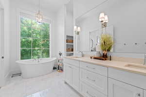 Freestanding soaking tub beneath a large window, complemented by a dual vanity with light-toned countertops, white cabinetry, and wall-mounted sconces