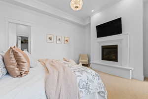 Recessed fireplace with a framed mantel and hearth, tray ceiling with crown molding, and a chandelier-style light fixture