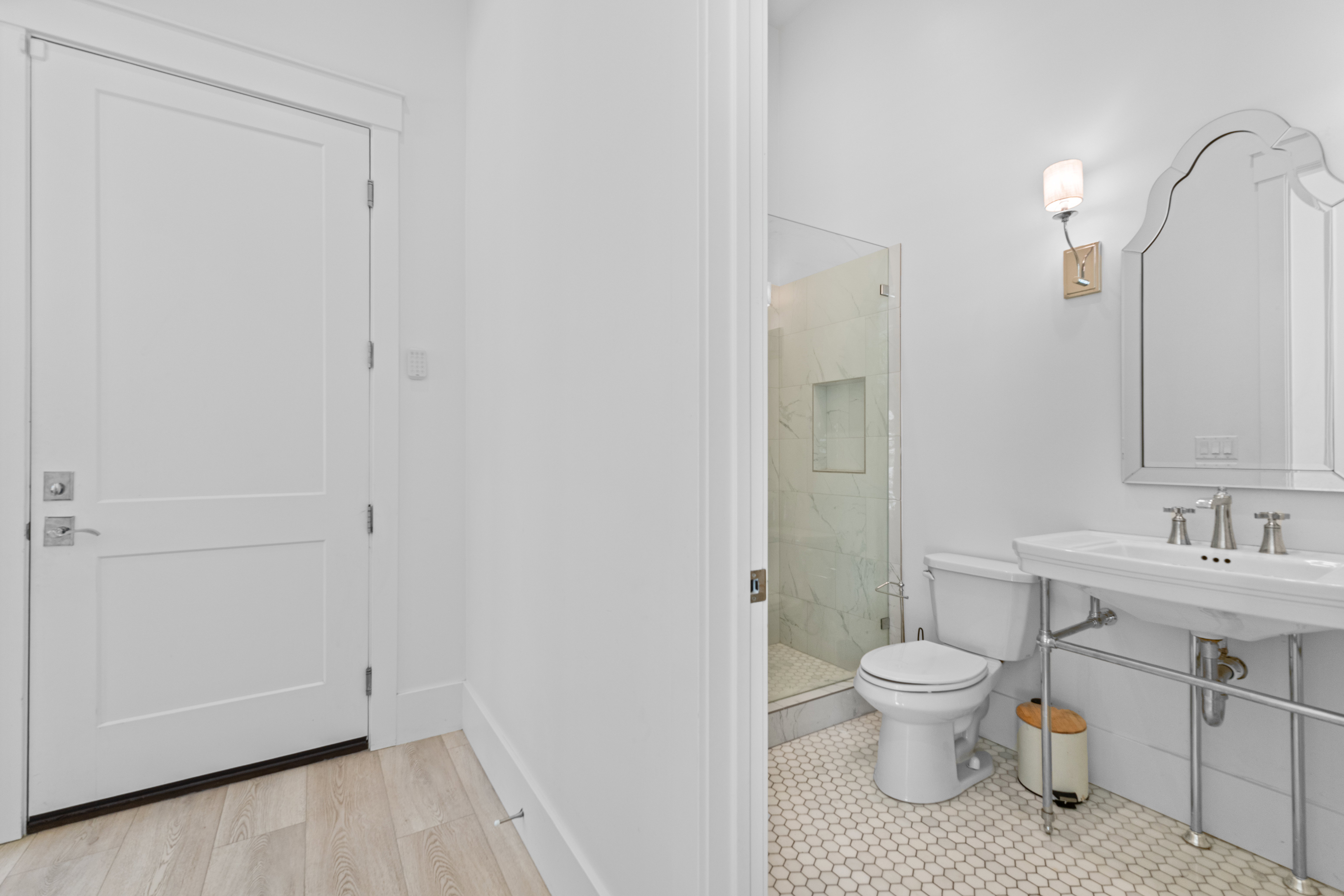 Bathroom featuring a white pedestal sink, frameless glass shower enclosure, white hexagon floor tiling, and a decorative wall mirror