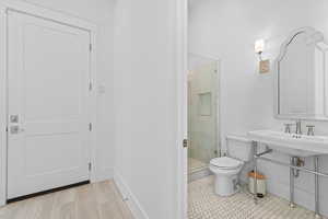 Bathroom featuring a white pedestal sink, frameless glass shower enclosure, white hexagon floor tiling, and a decorative wall mirror