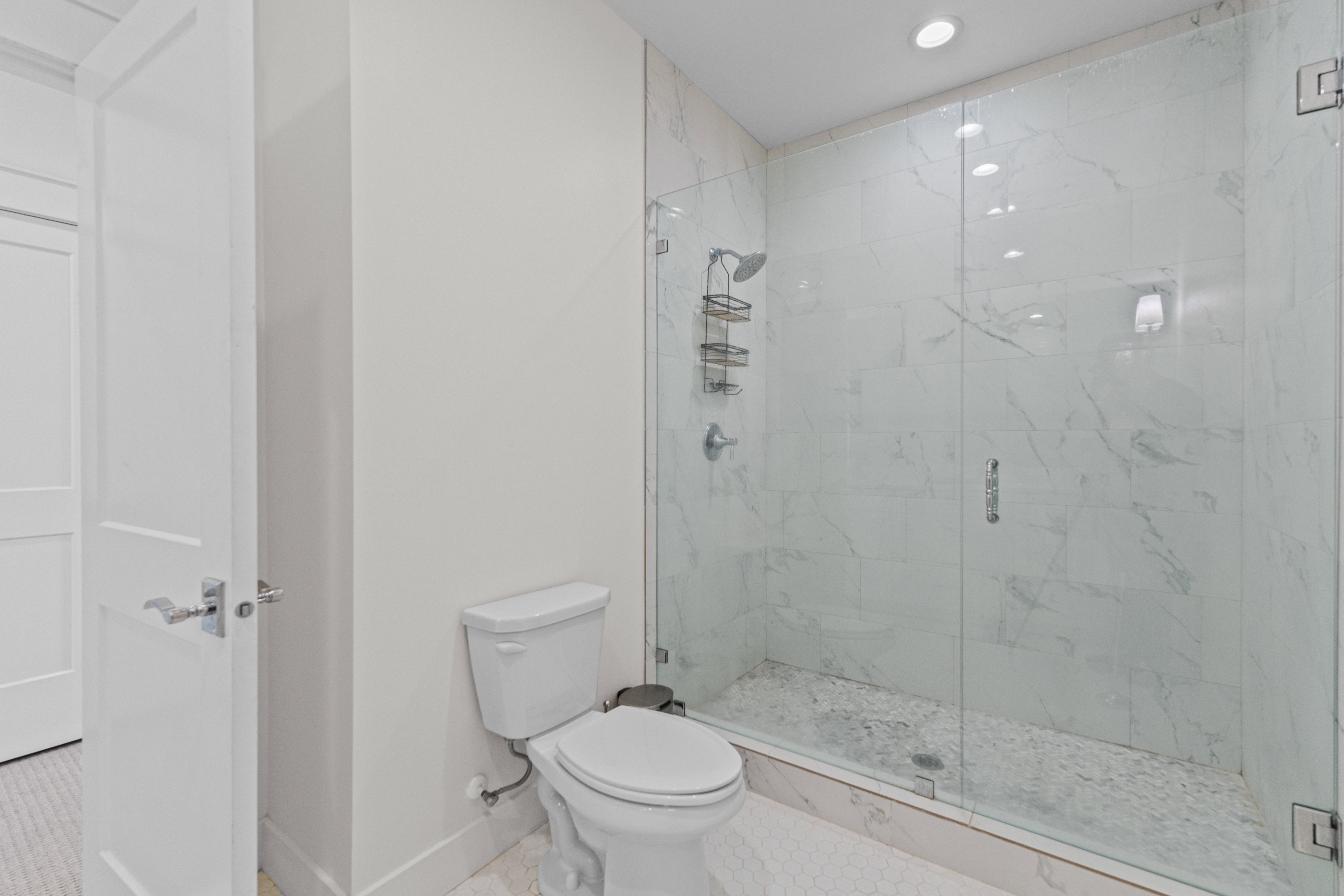 Walk-in shower with clear glass enclosure, white marbled tile surround, and pebble stone floor
