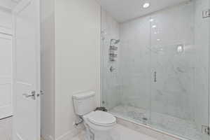 Walk-in shower with clear glass enclosure, white marbled tile surround, and pebble stone floor