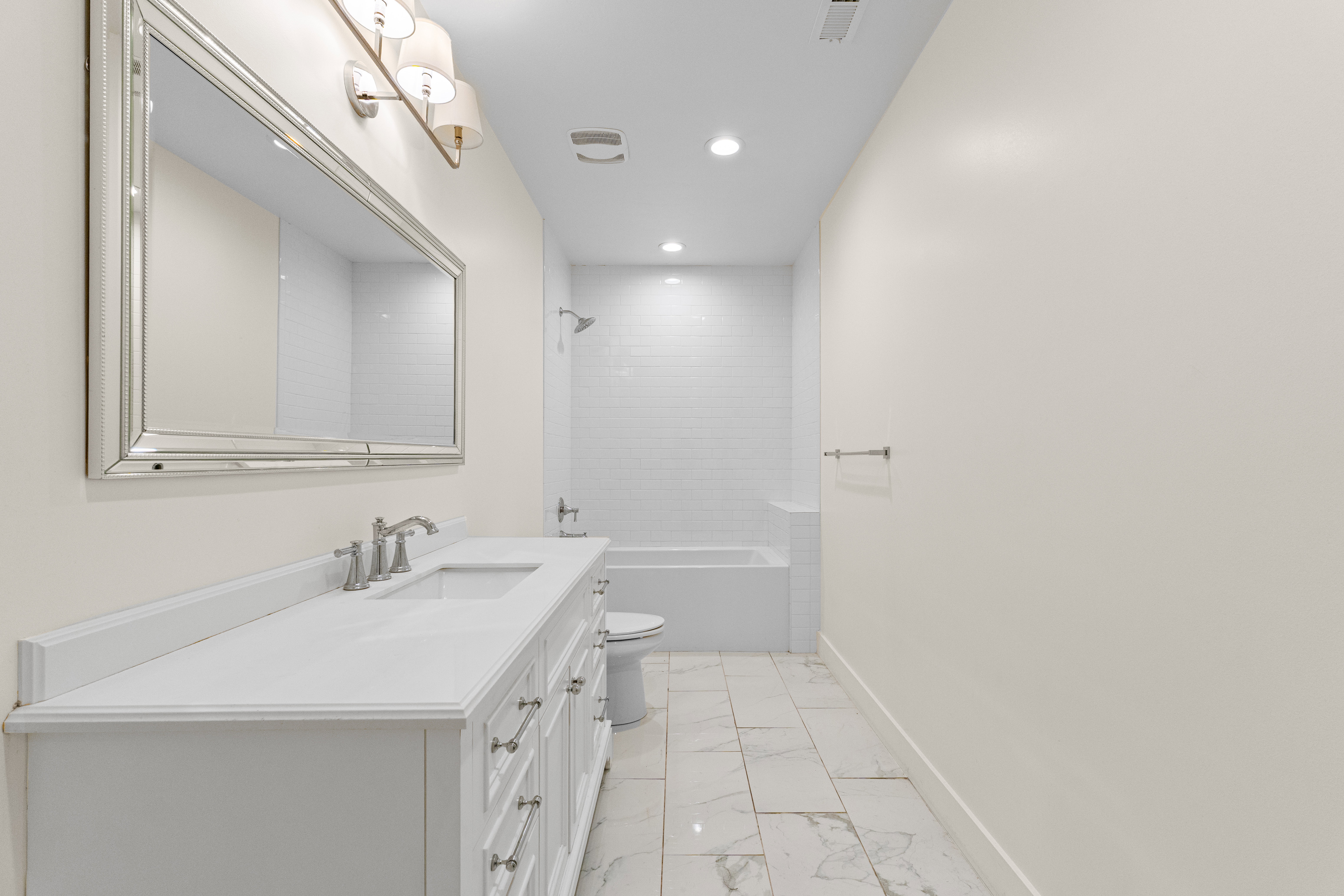 White vanity with a single basin, brushed nickel faucet, and a large framed mirror with sconce lighting