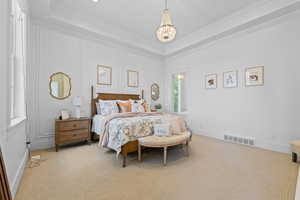 Spacious bedroom featuring tray ceilings, a chandelier, wall paneling, and neutral carpeting