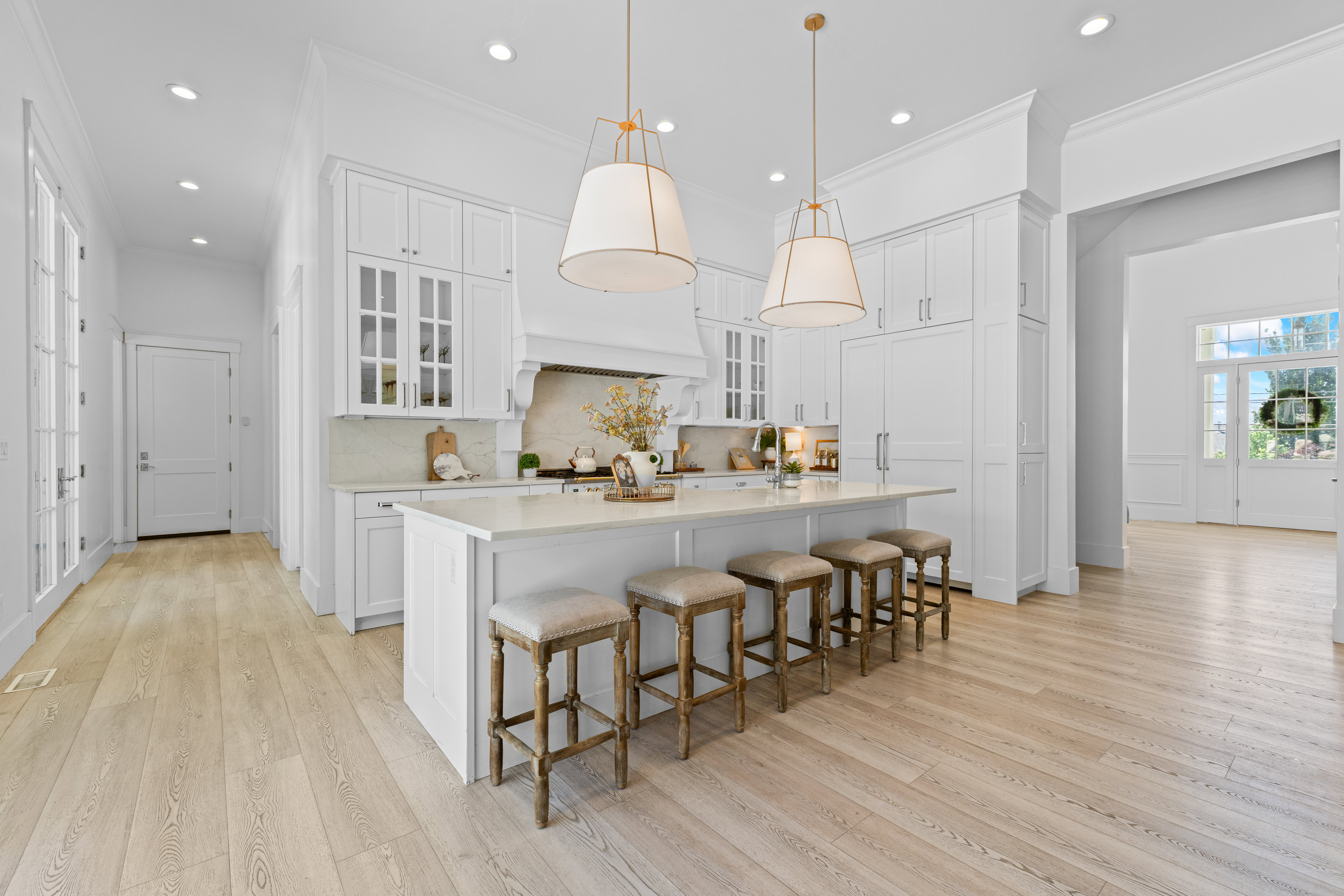 Expansive kitchen featuring white cabinetry, a large center island with seating, pendant lighting, built-in appliances, and light wood-finish flooring