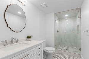 Bathroom featuring a frameless glass shower enclosure with marble-patterned tile, a white vanity with drawers, a single basin sink, and a decorative framed mirror