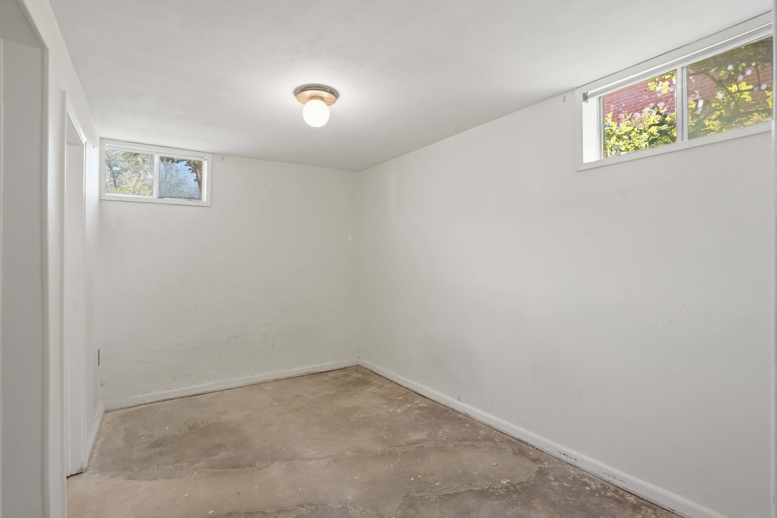 Brightly lit room featuring two windows, a ceiling-mounted light fixture, and concrete flooring