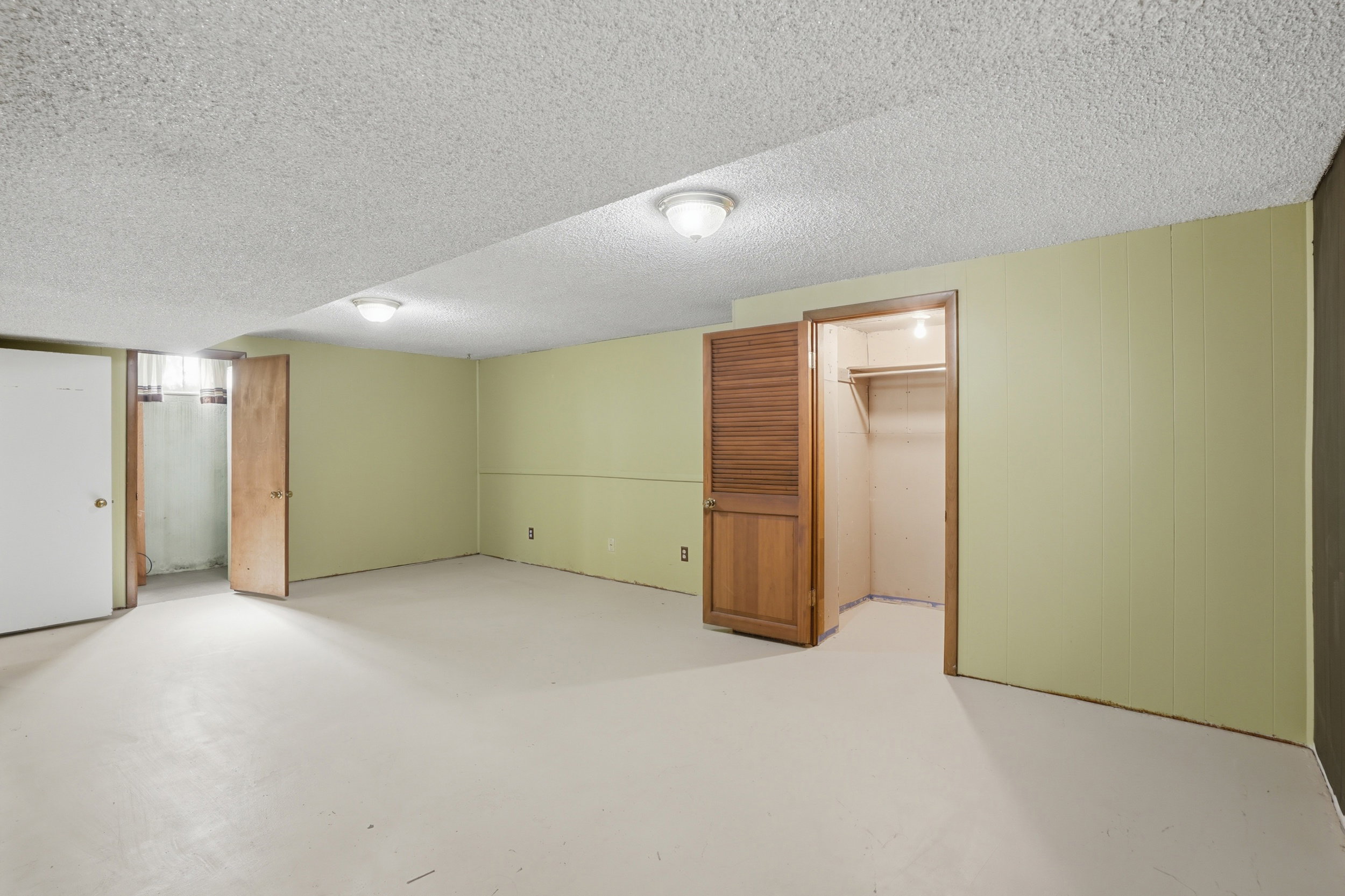 Spacious room featuring light green paneling, a textured ceiling, flush-mount lighting, and a closet with a louvered bi-fold door