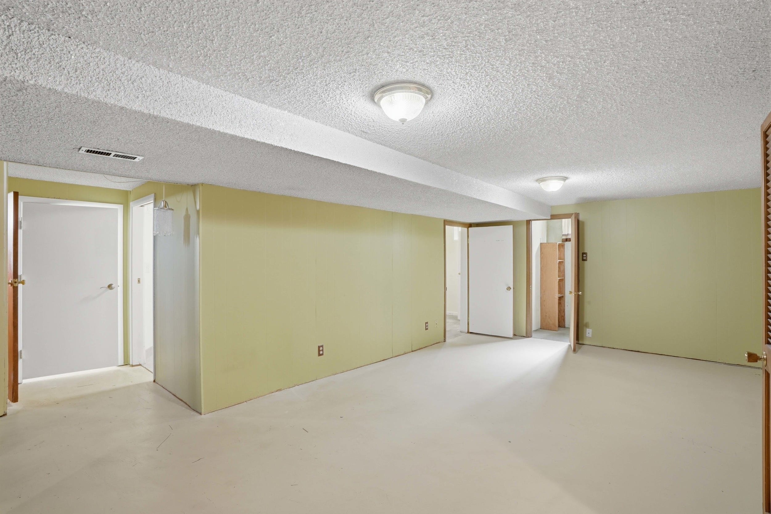 Expansive room featuring light-toned walls, multiple doorways, and overhead lighting