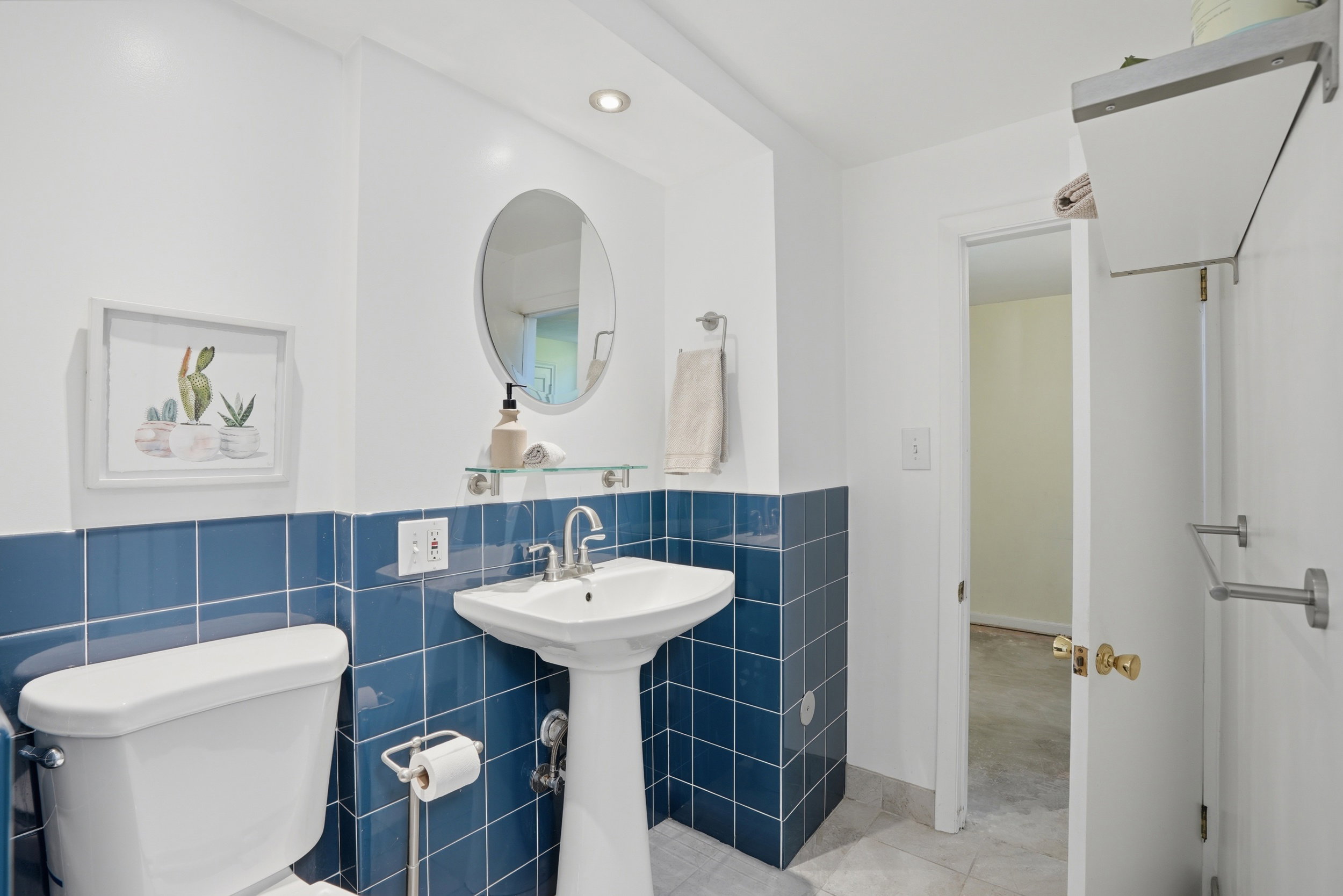 Pedestal sink with chrome faucet, complemented by a round mirror and a glass shelf