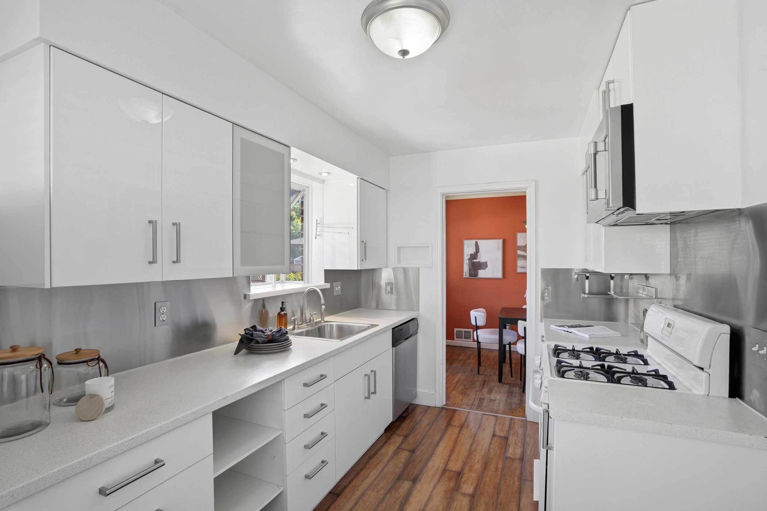 Kitchen featuring white cabinetry, stainless steel appliances, a stainless steel backsplash, and wood-finish flooring