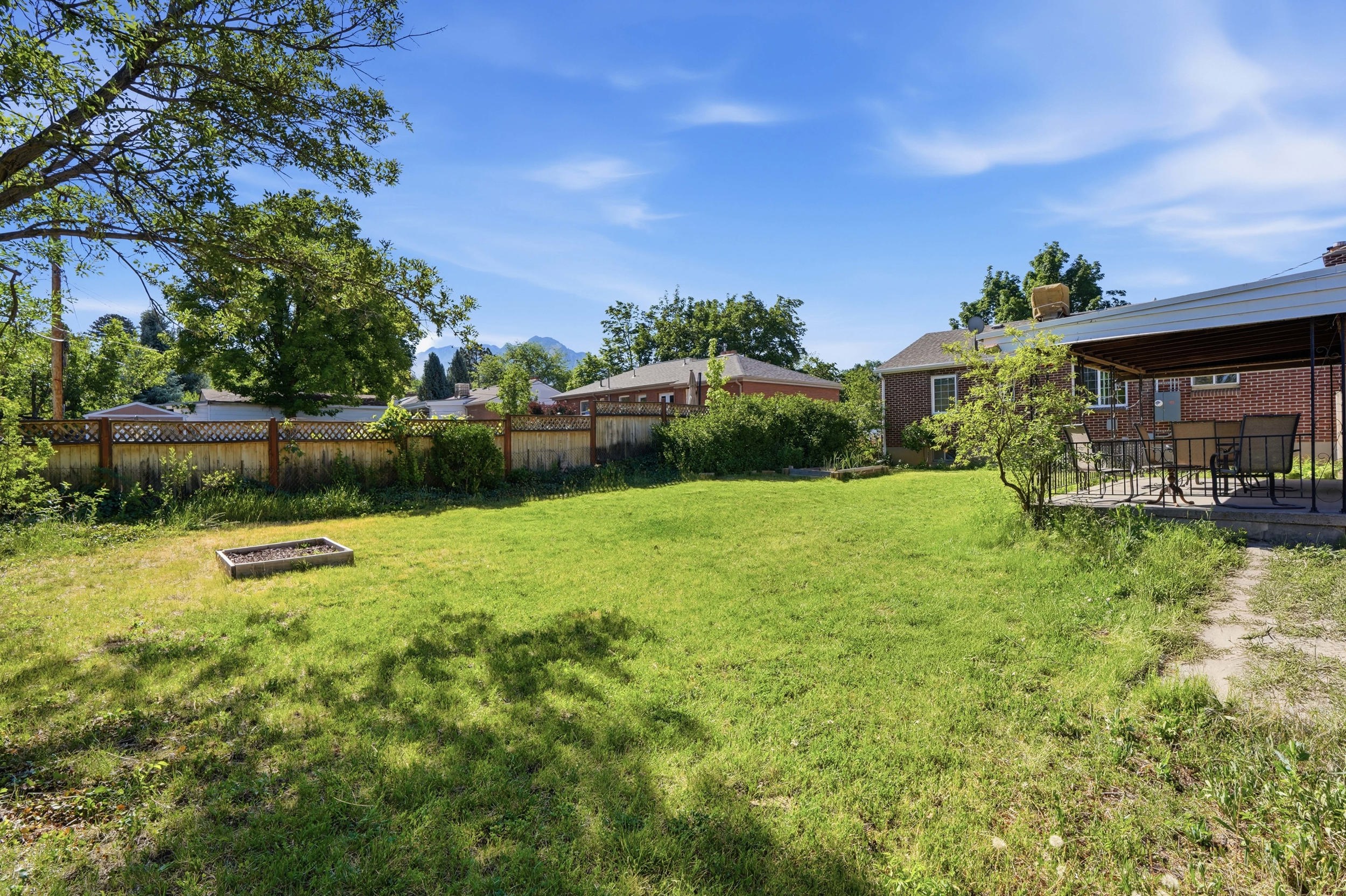 Expansive backyard featuring a large grassy area, a raised garden bed, and a covered patio with a paved surface