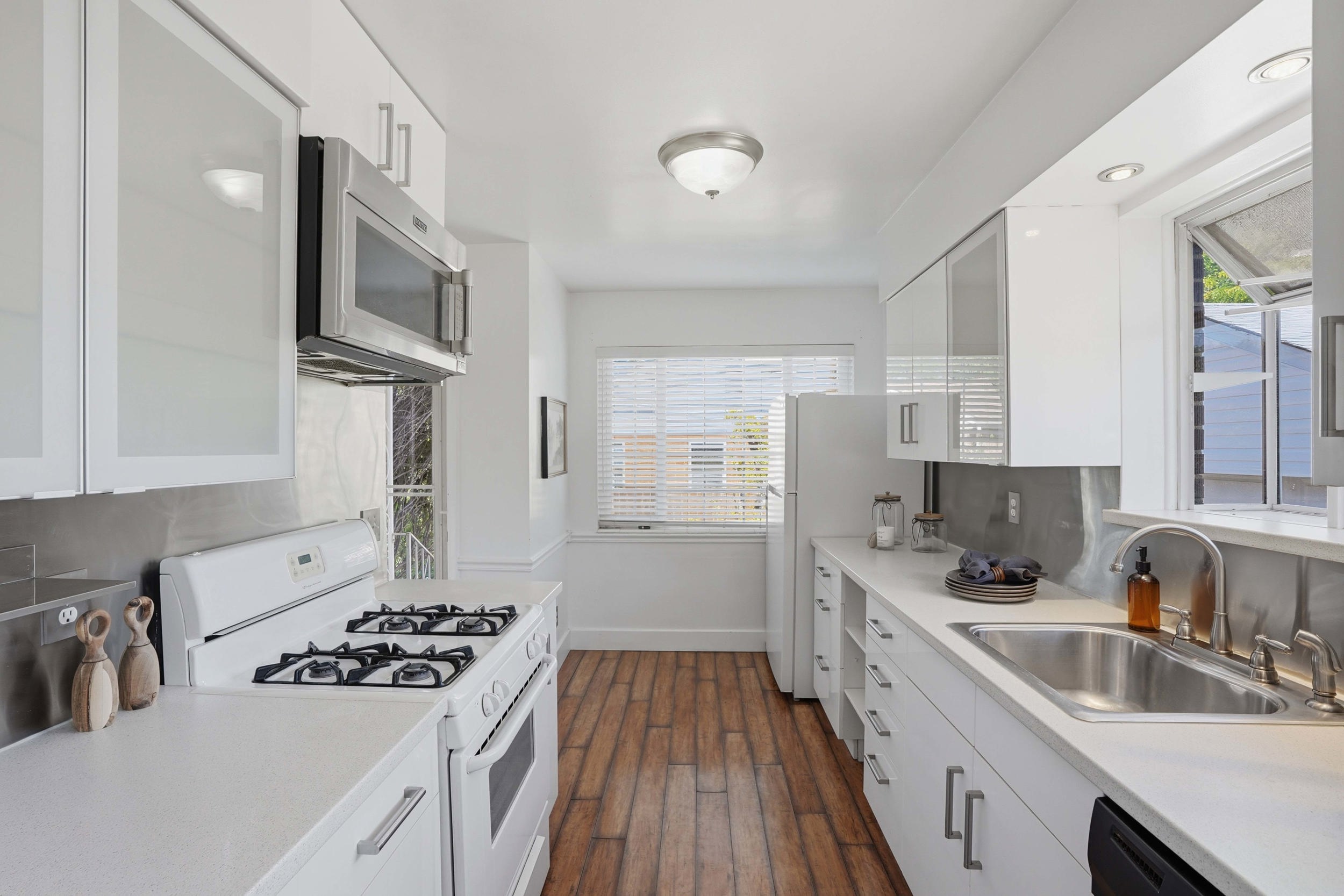 Bright kitchen featuring white cabinetry, stainless steel appliances, wood-finish flooring, and a stainless steel backsplash