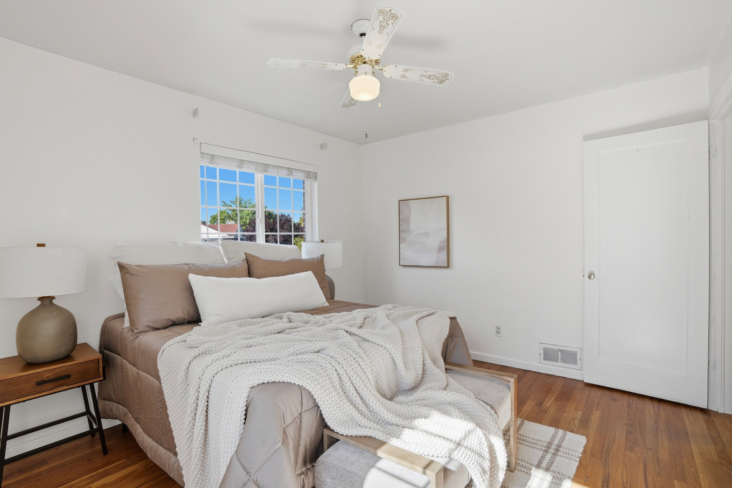 Bright room featuring wood-finish flooring, a multi-pane window, and a ceiling fan with integrated lighting