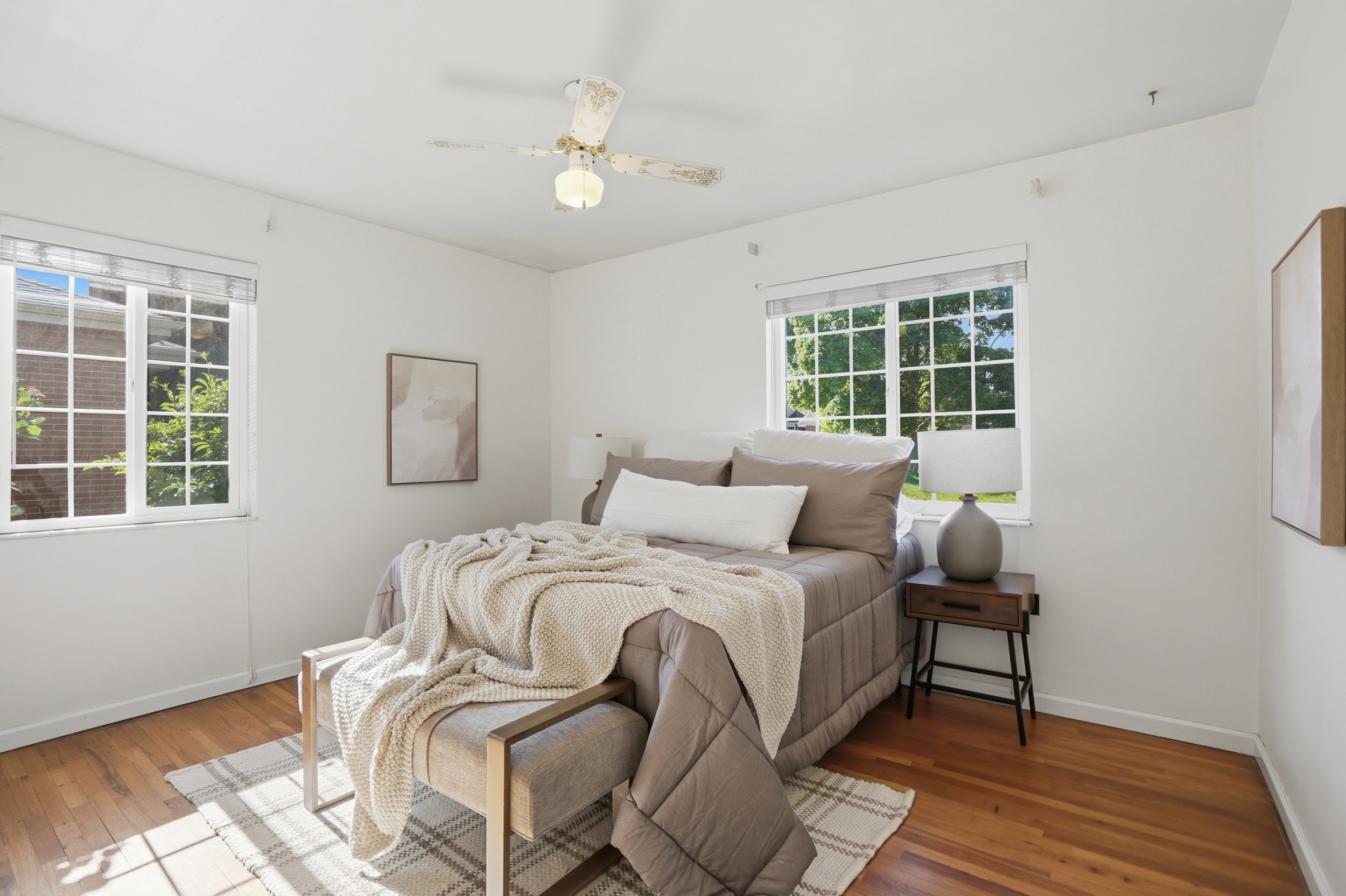Bright room featuring two multi-pane windows, wood-finish flooring, a ceiling fan with light fixture, and white wall finishes