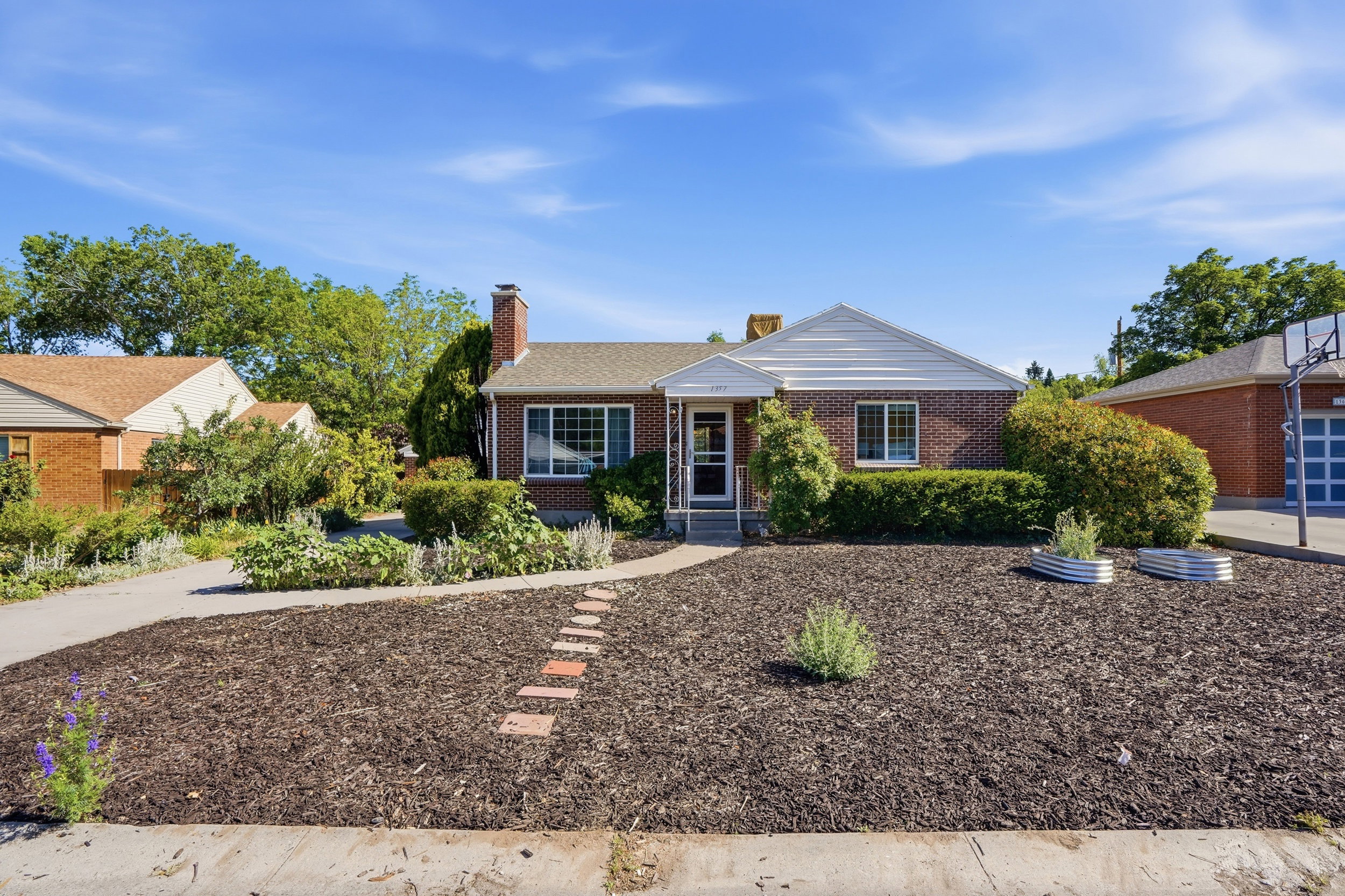 Brick exterior with a gable roofline, mature landscaping, and a driveway