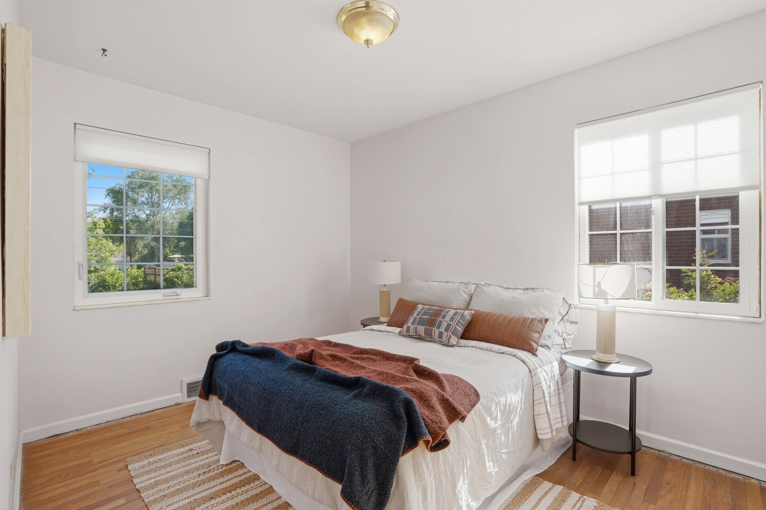 Bedroom featuring wood-finish flooring, two large windows with roller shades, and a flush-mount ceiling light fixture