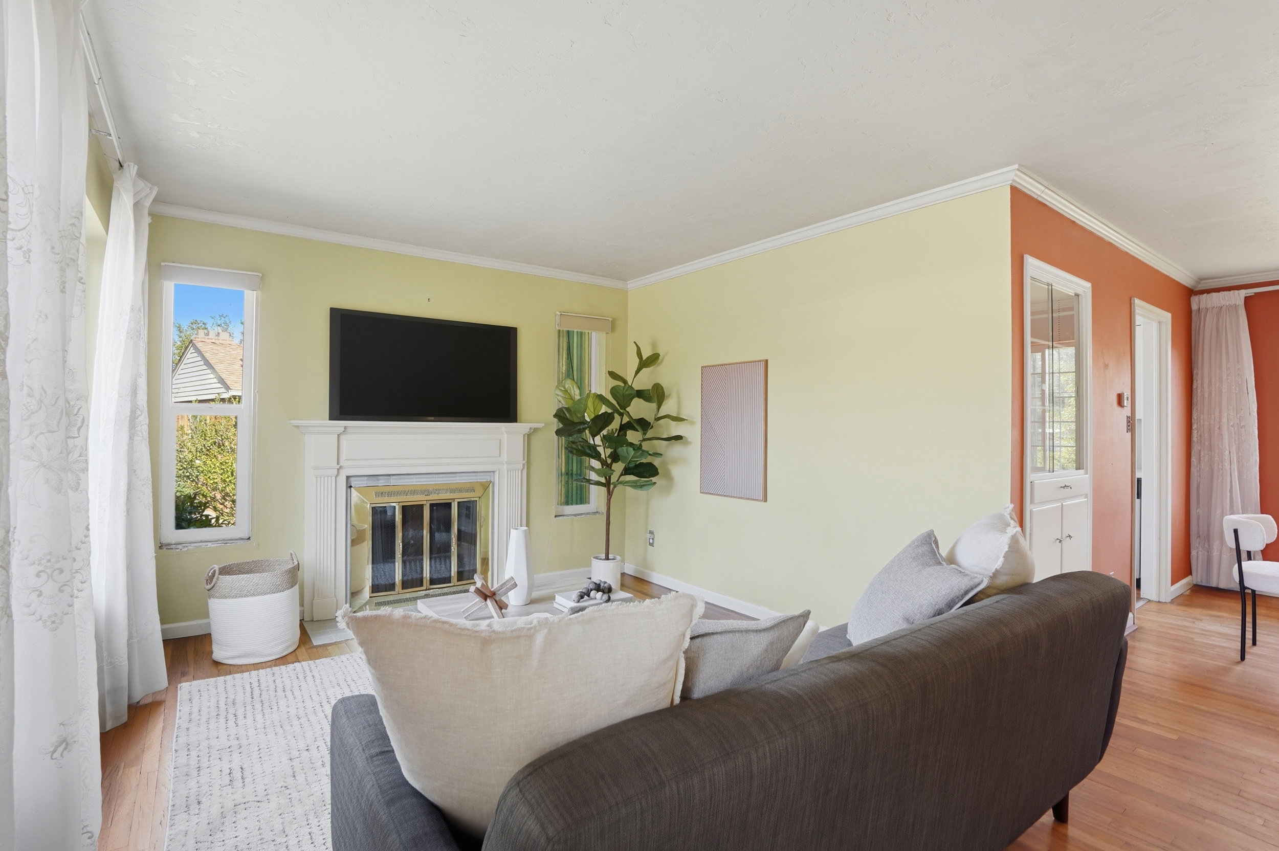 Living area featuring a classic white fireplace mantel with brass-toned insert, wood-finish flooring, two-tone wall paint, and multiple windows providing natural light