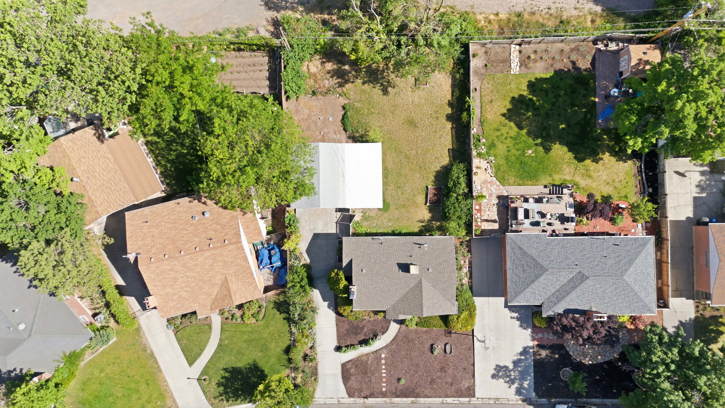 Aerial perspective showcasing a residential property with a multi-level deck, fenced backyard, and established landscaping