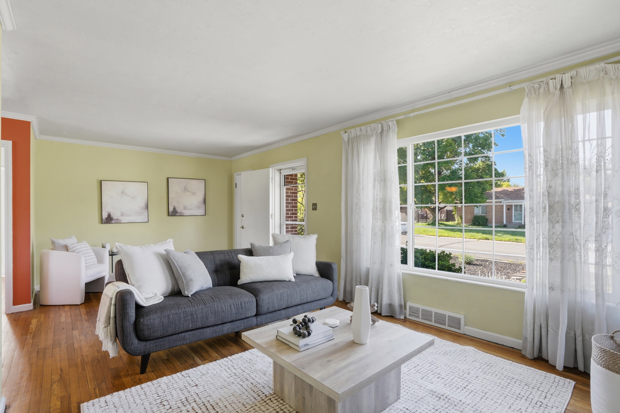 Living area featuring a large picture window with multiple panes, hardwood flooring, light-colored walls, crown molding, and a white entry door