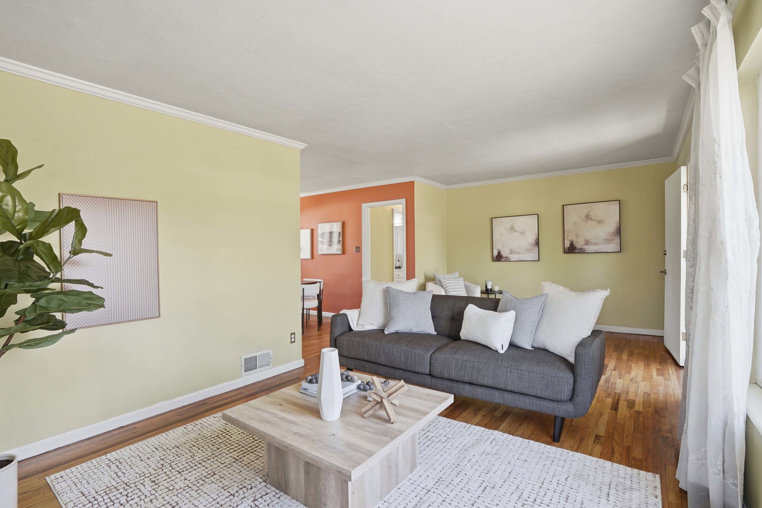 Living area featuring wood-finish flooring, light yellow painted walls, white baseboards, and crown molding