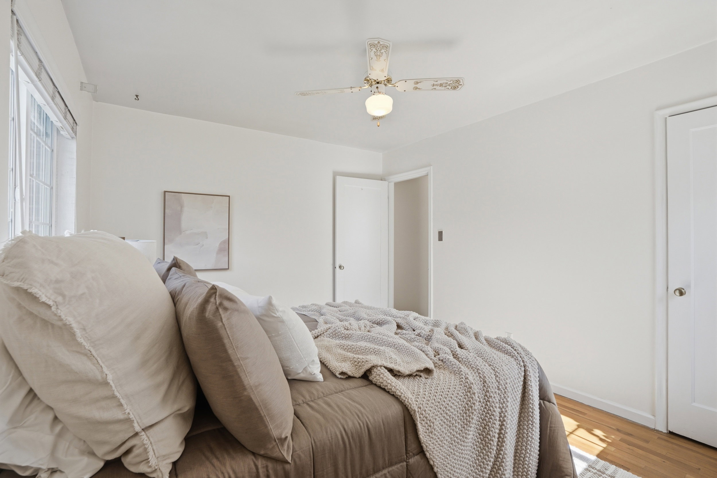Light-filled room featuring hardwood flooring and a white ceiling fan