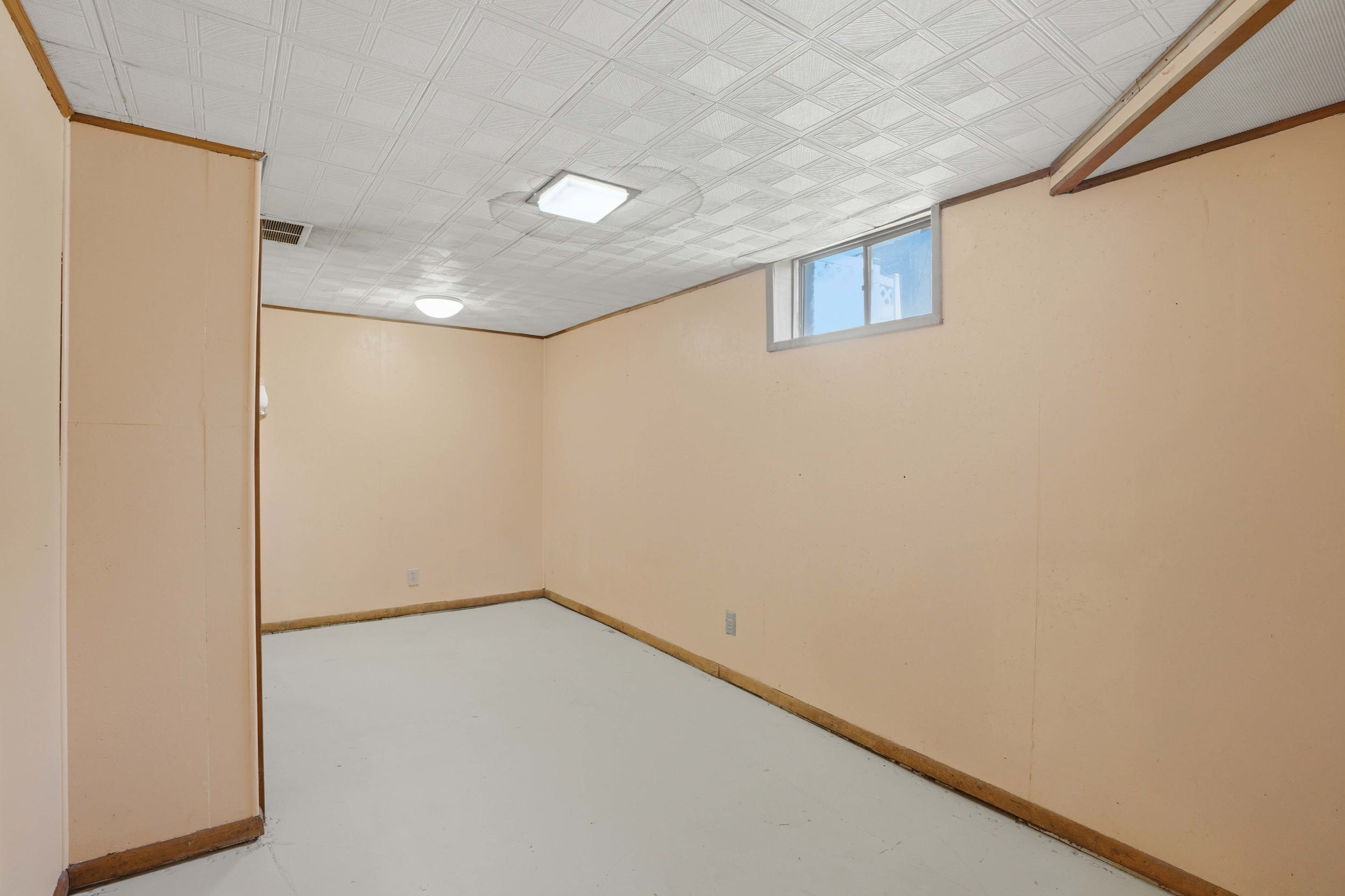 Finished room featuring light-colored walls and flooring, a drop ceiling, and an egress window