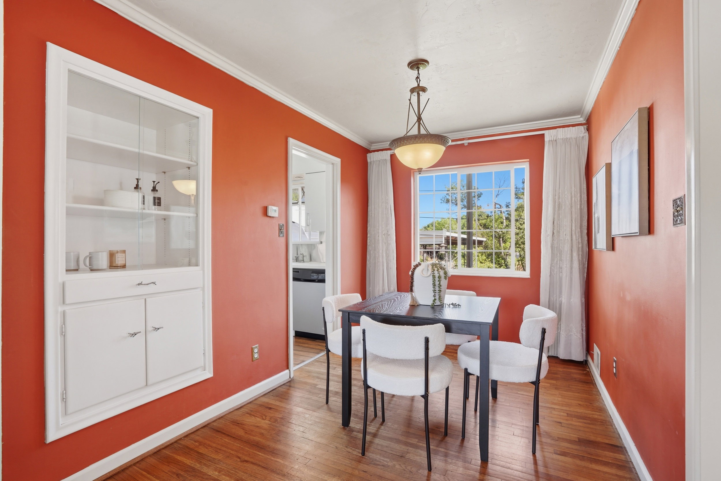 Dining space featuring wood-finish flooring, built-in cabinetry with glass-front uppers, crown molding, and a prominent window