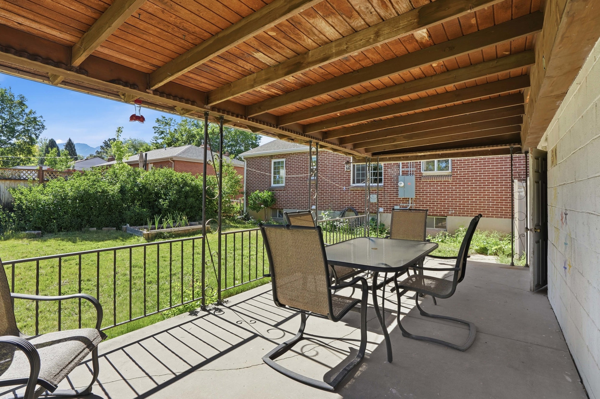 Covered concrete patio with a wood-plank ceiling, black metal railing, and an expansive lawn