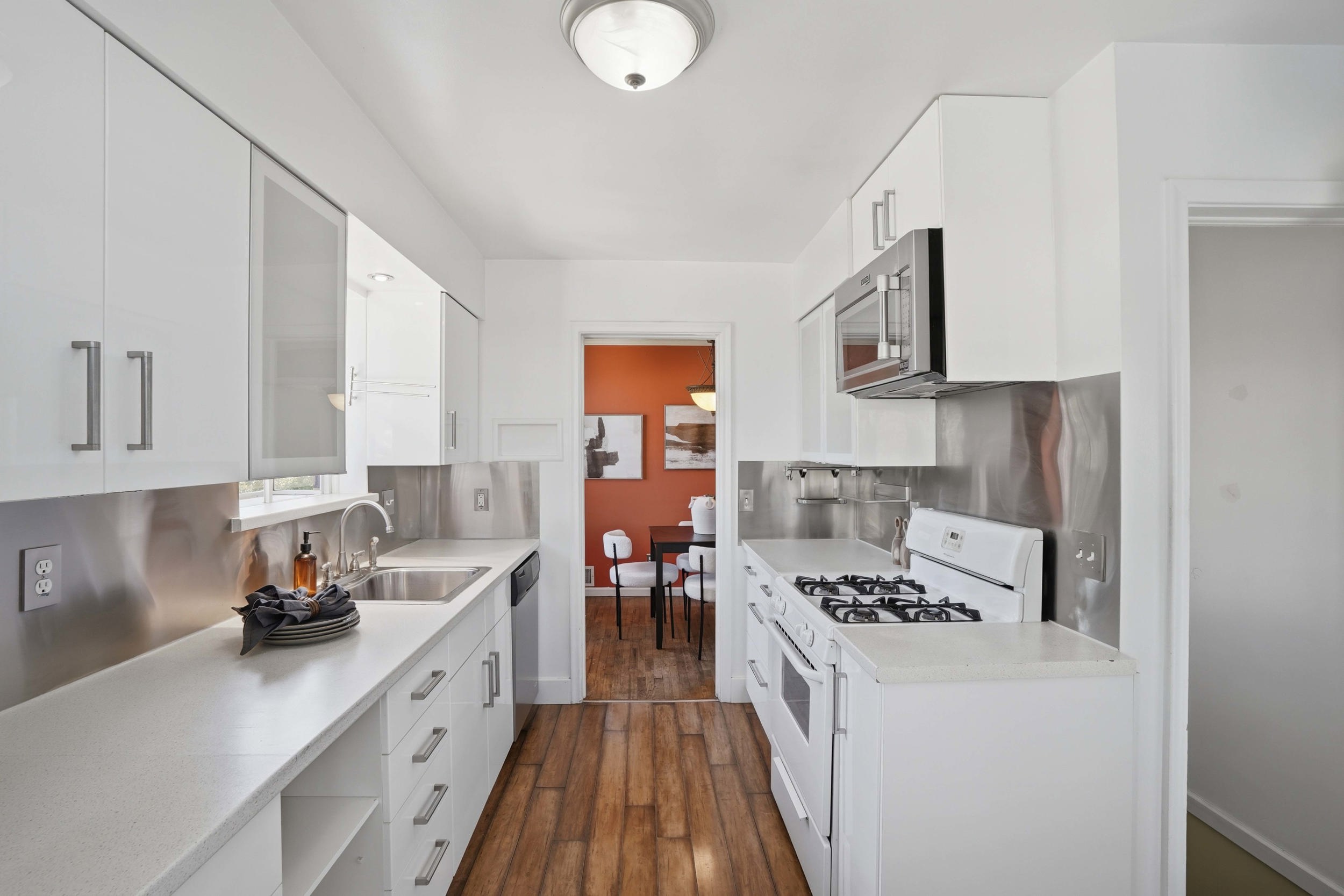 Galley kitchen featuring white cabinetry, light-toned countertops, and wood-finish flooring
