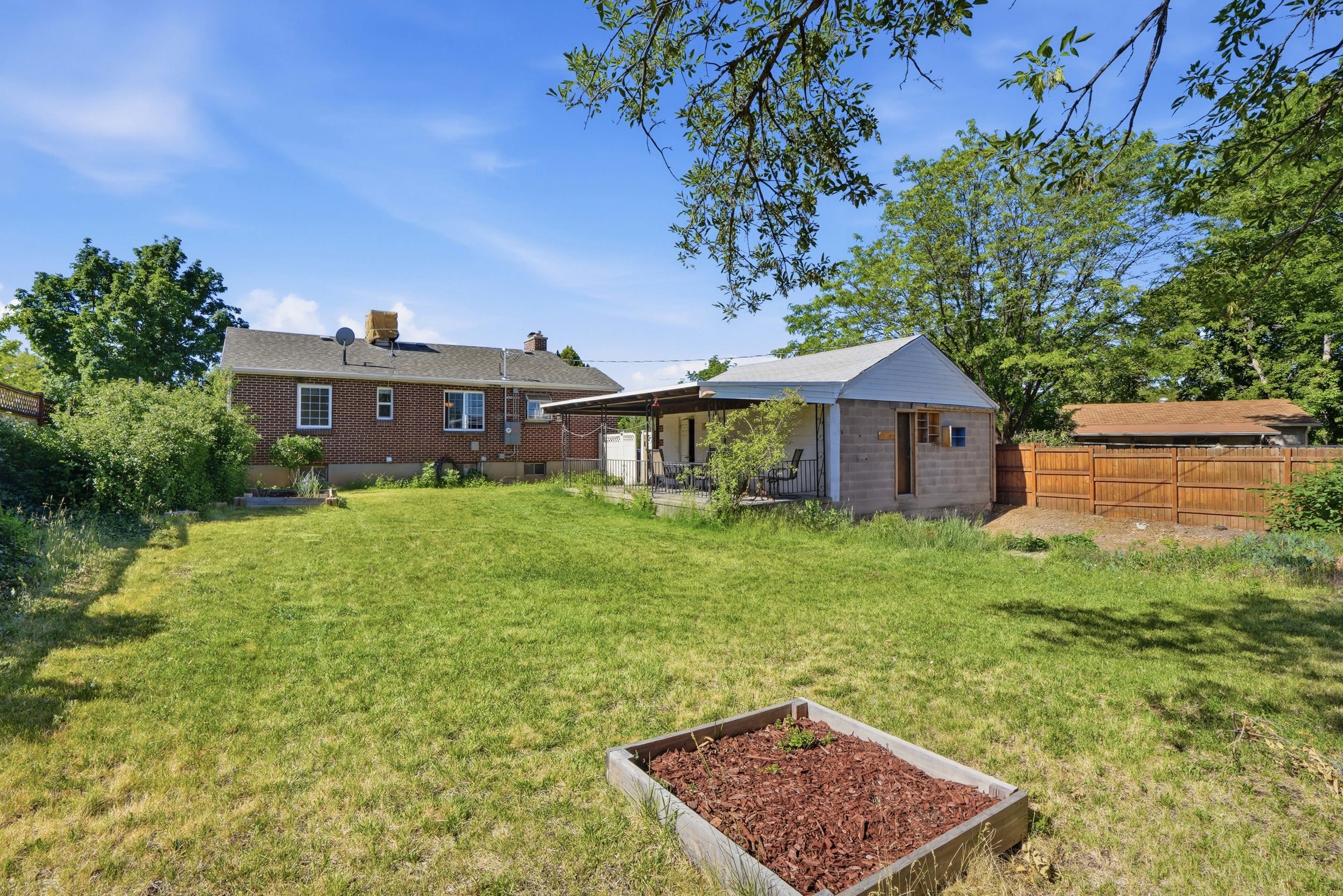 Expansive backyard featuring a large grass area, wood-fenced perimeter, and a raised garden bed