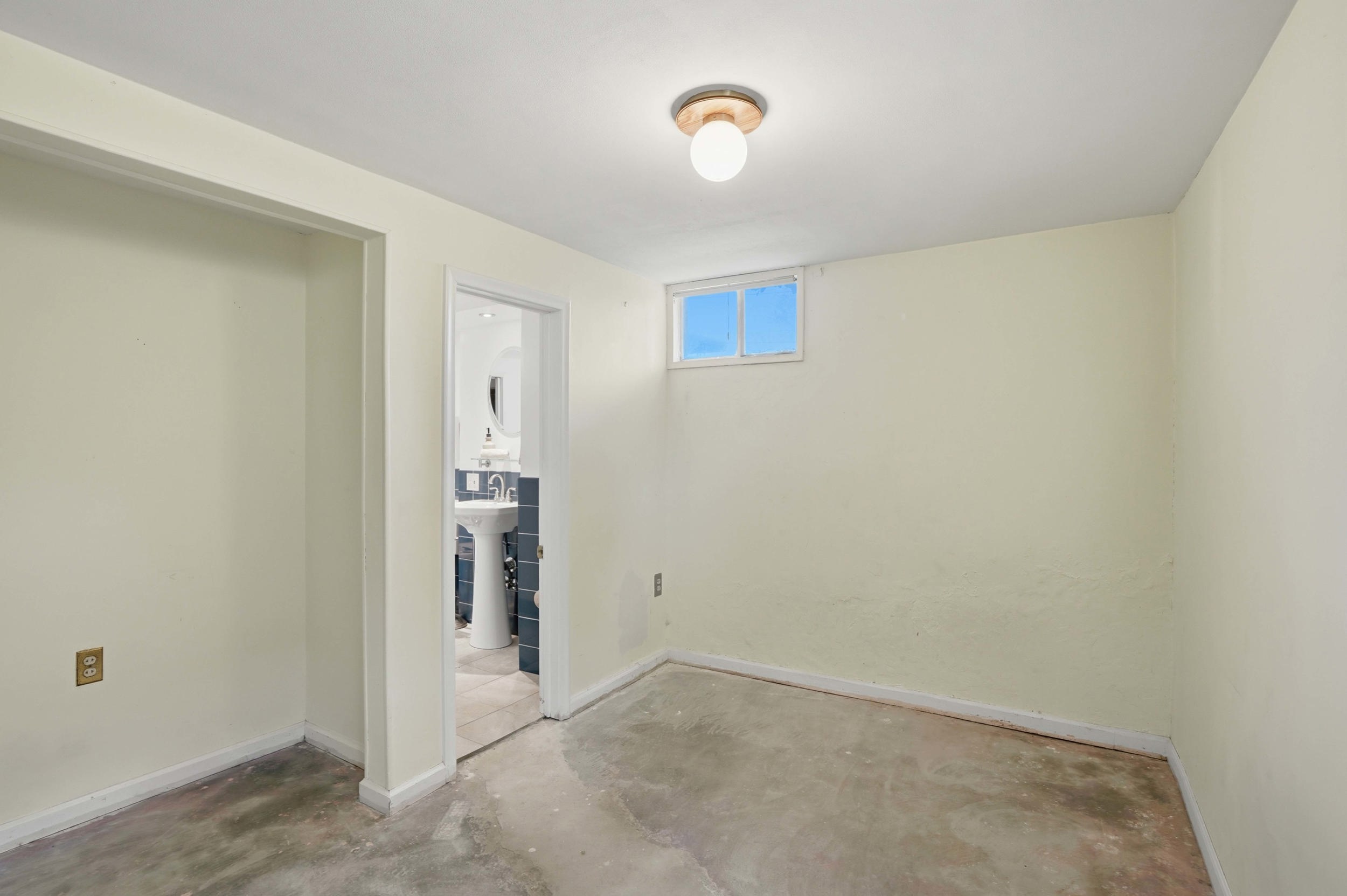 Spacious room featuring light-toned walls, a single window, and a ceiling-mounted light fixture