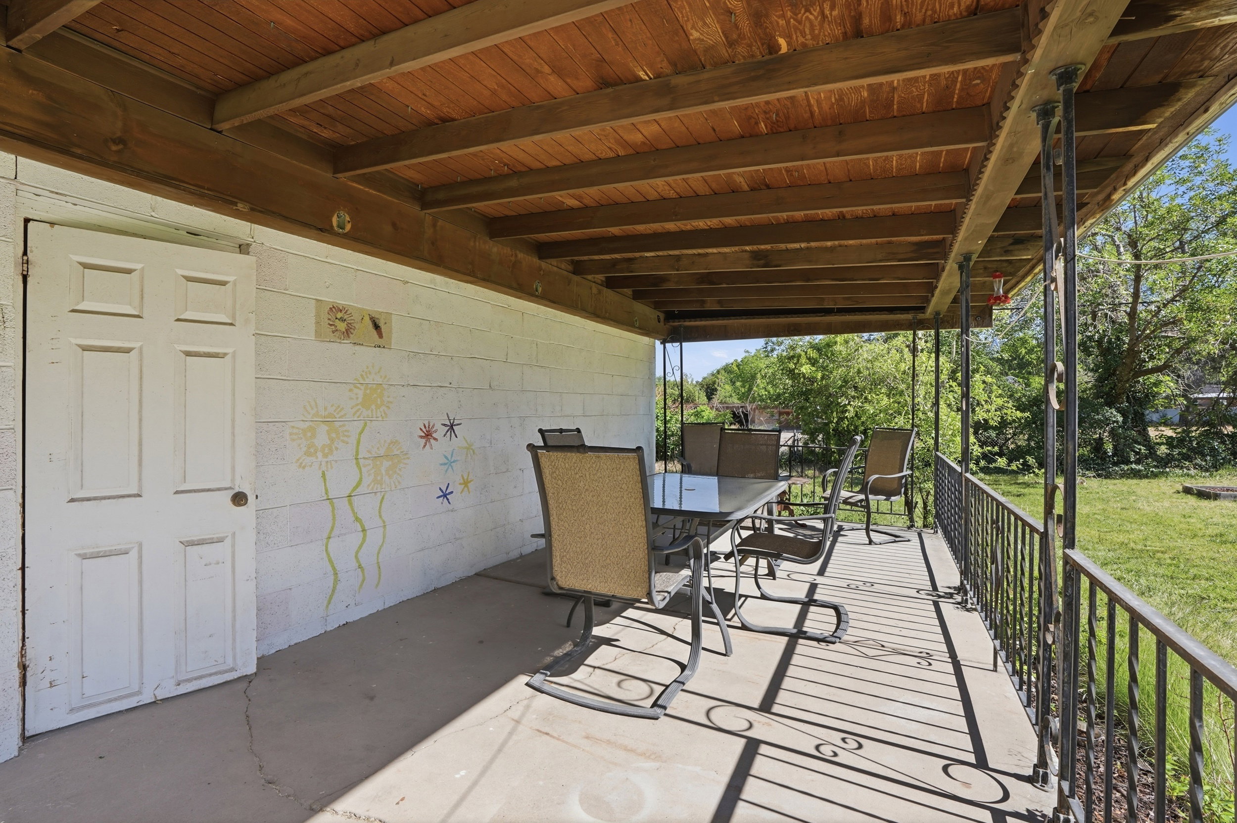 Covered concrete patio featuring a wood-panel ceiling and decorative wrought iron railing