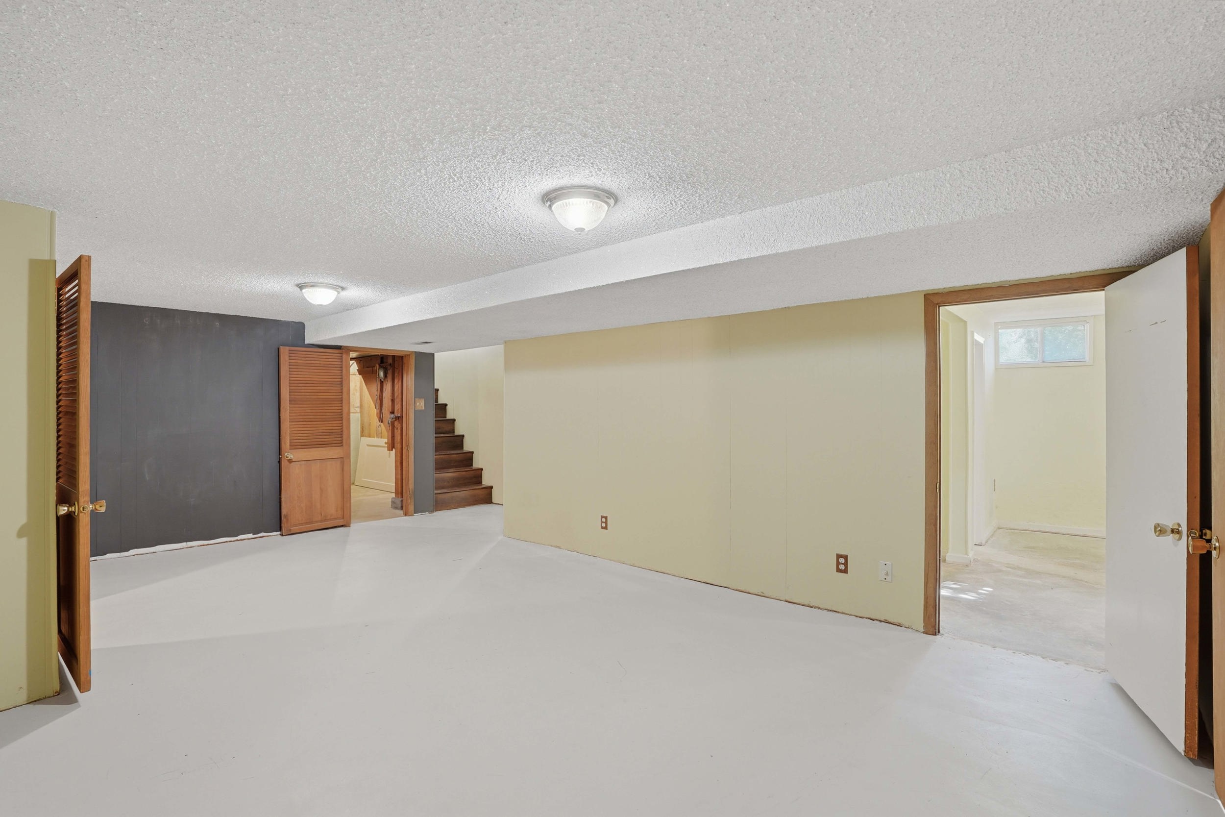 Spacious lower level featuring light-colored flooring, neutral wall tones, multiple entryways, overhead lighting, and visible stairs
