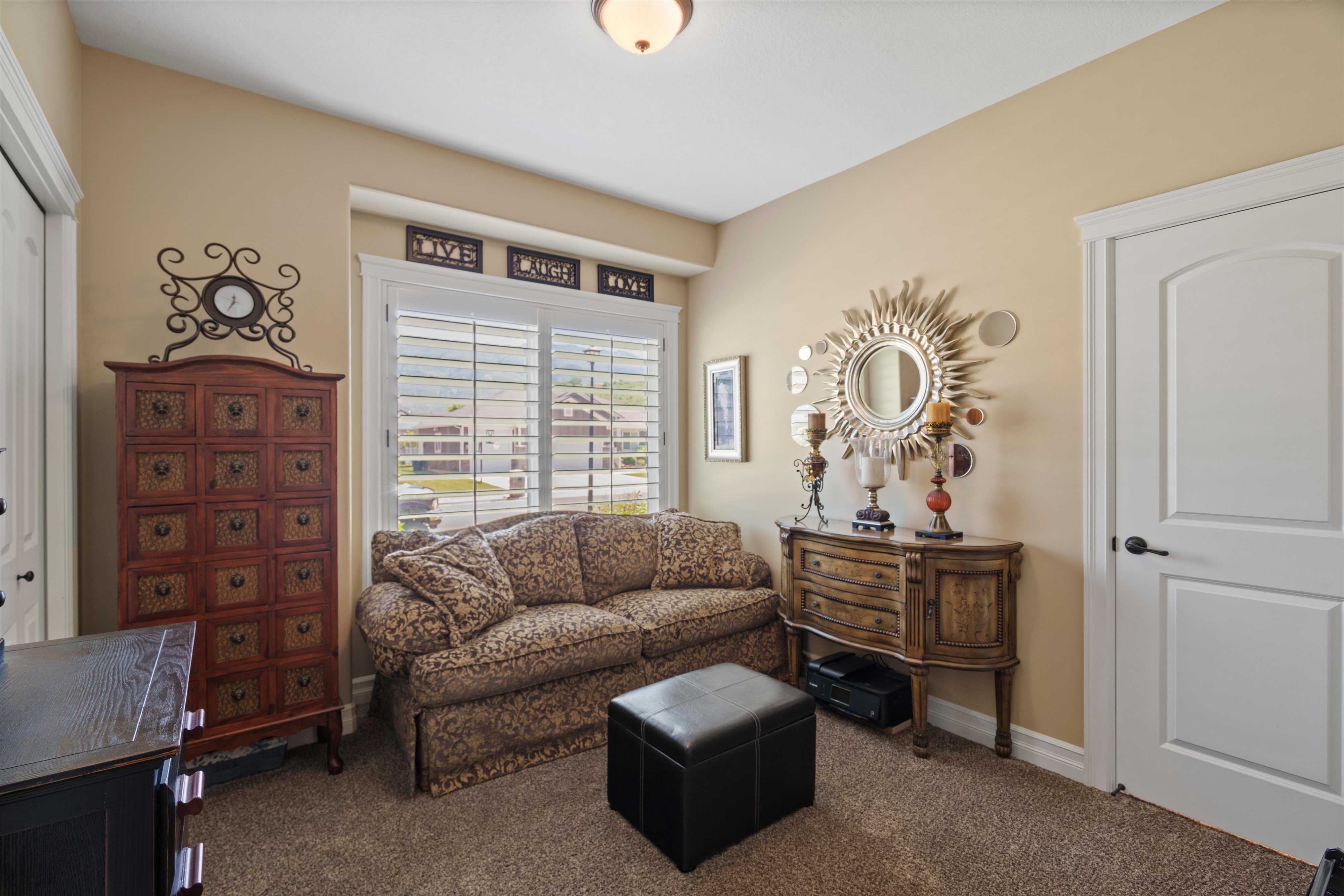 Carpeted room featuring a window with white plantation shutters, a white paneled door with black hardware, and light beige wall paint